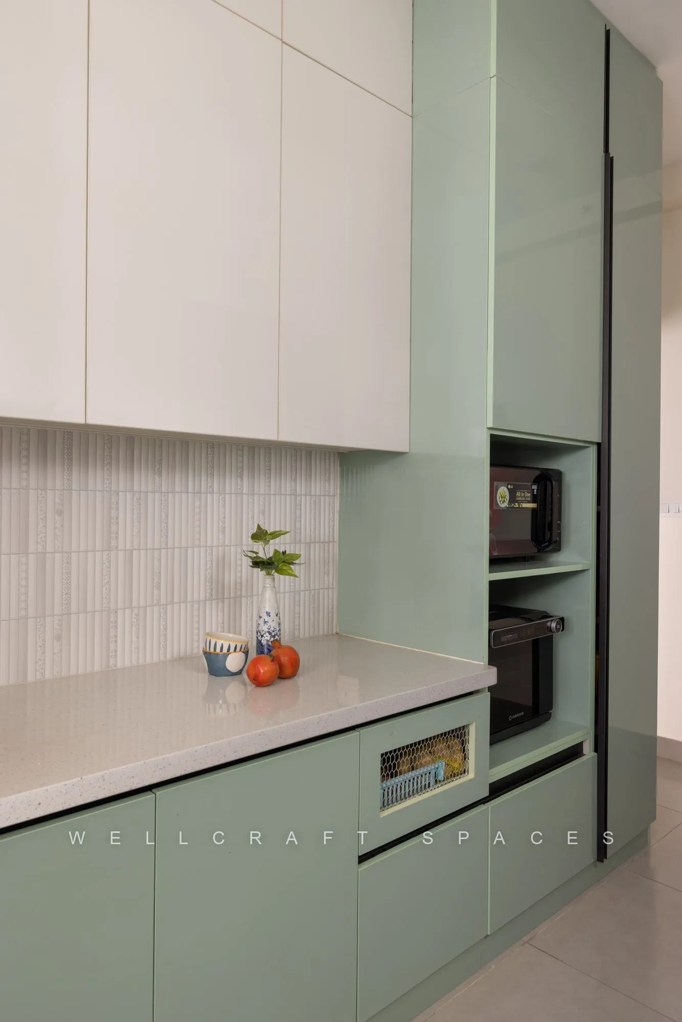 Tall sage cabinetry housing a built-in oven and microwave beside the stone counter and white wall units.