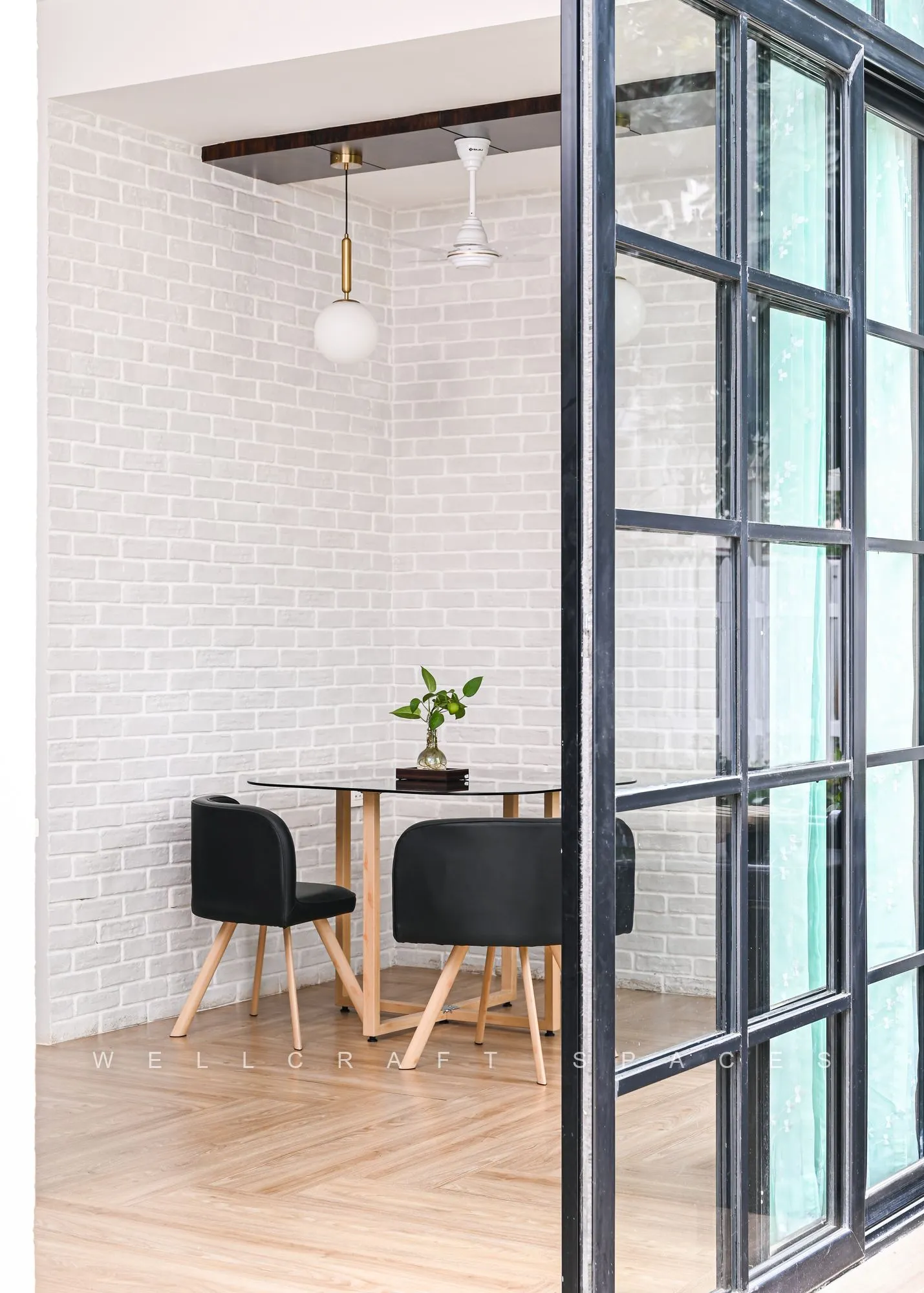Breakfast nook in pale oak and black metal, with two moulded chairs by black-framed glass doors opening onto the garden.