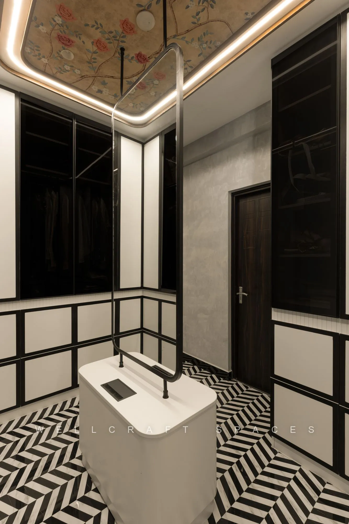 Walk-in wardrobe in black and gold framed glass with a central island drawer unit and a black-and-white chevron tile floor.
