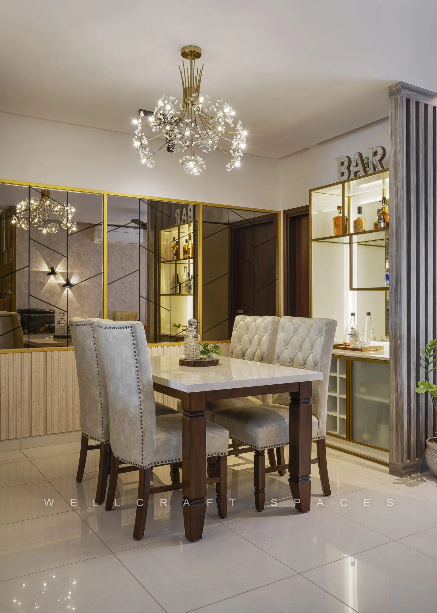 Dining setting beside a glass-fronted brass crockery unit, lit by a starburst chandelier over ivory floor tiles.