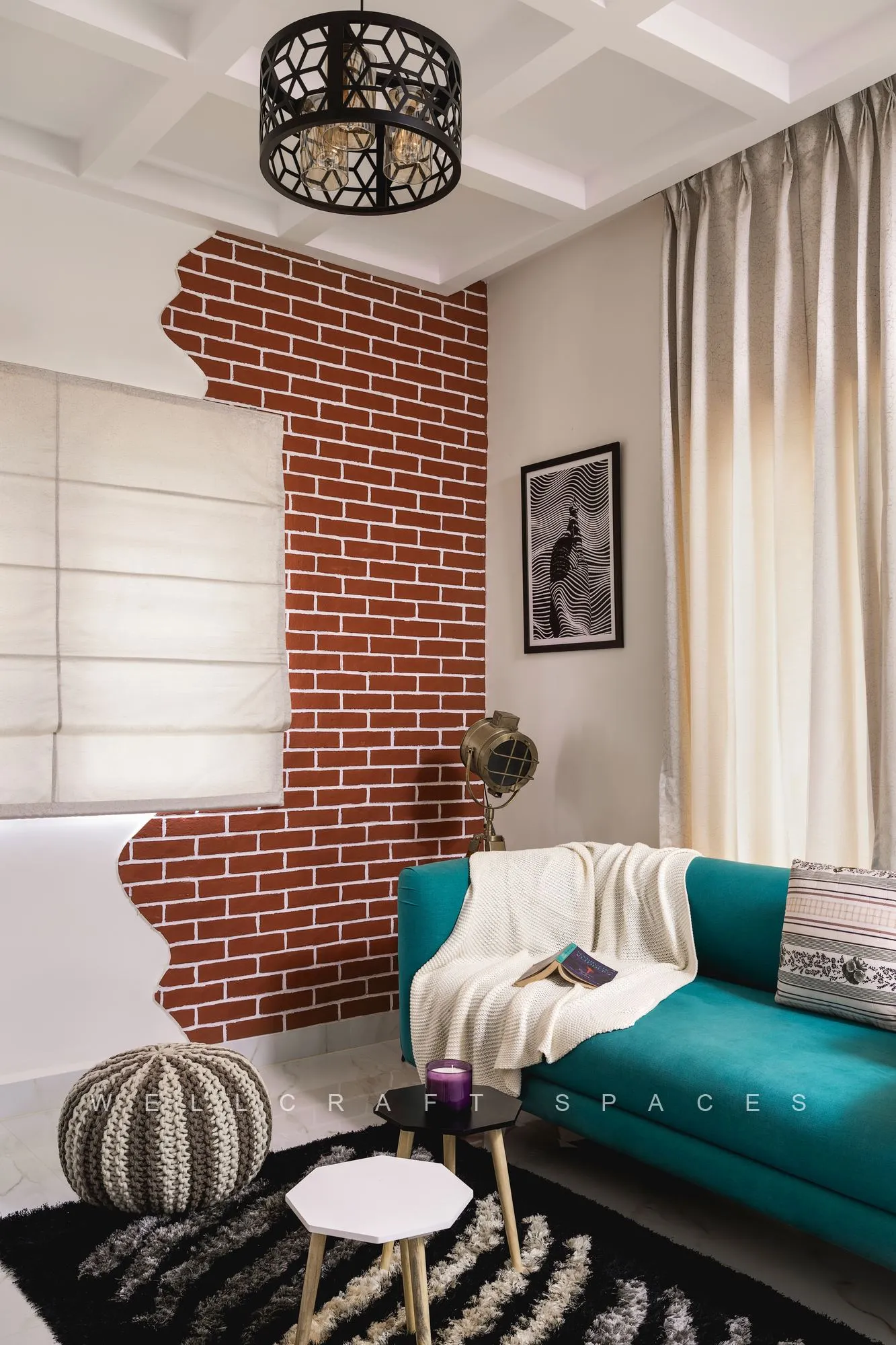 Family lounge with a teal sofa against an exposed red brick column, a coffered ceiling with a perforated black drum light, a knitted pouffe and a monochrome patterned rug.