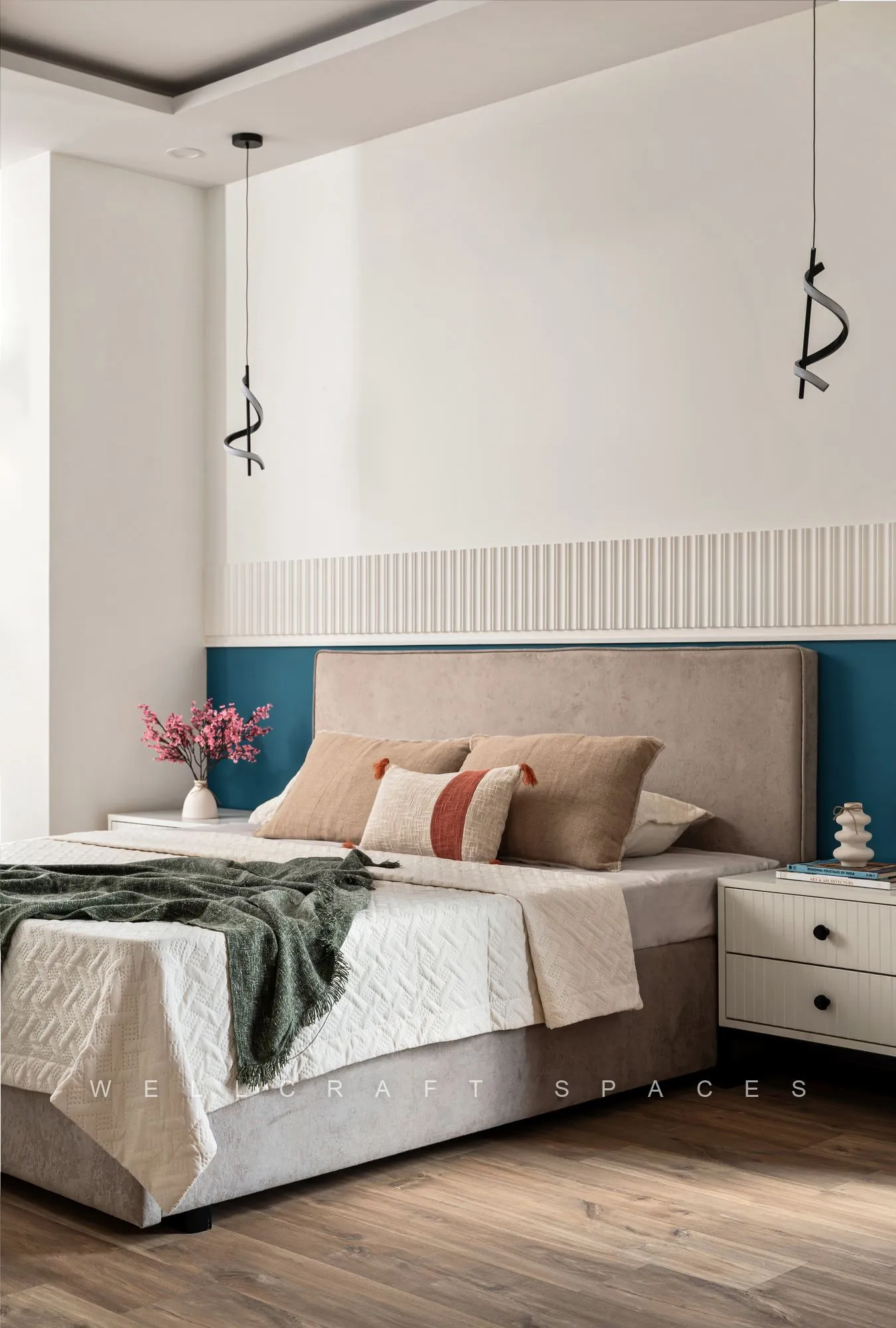 Bed with an upholstered beige headboard against a teal panelled wall, layered with olive and rust bedding over oak-toned flooring.