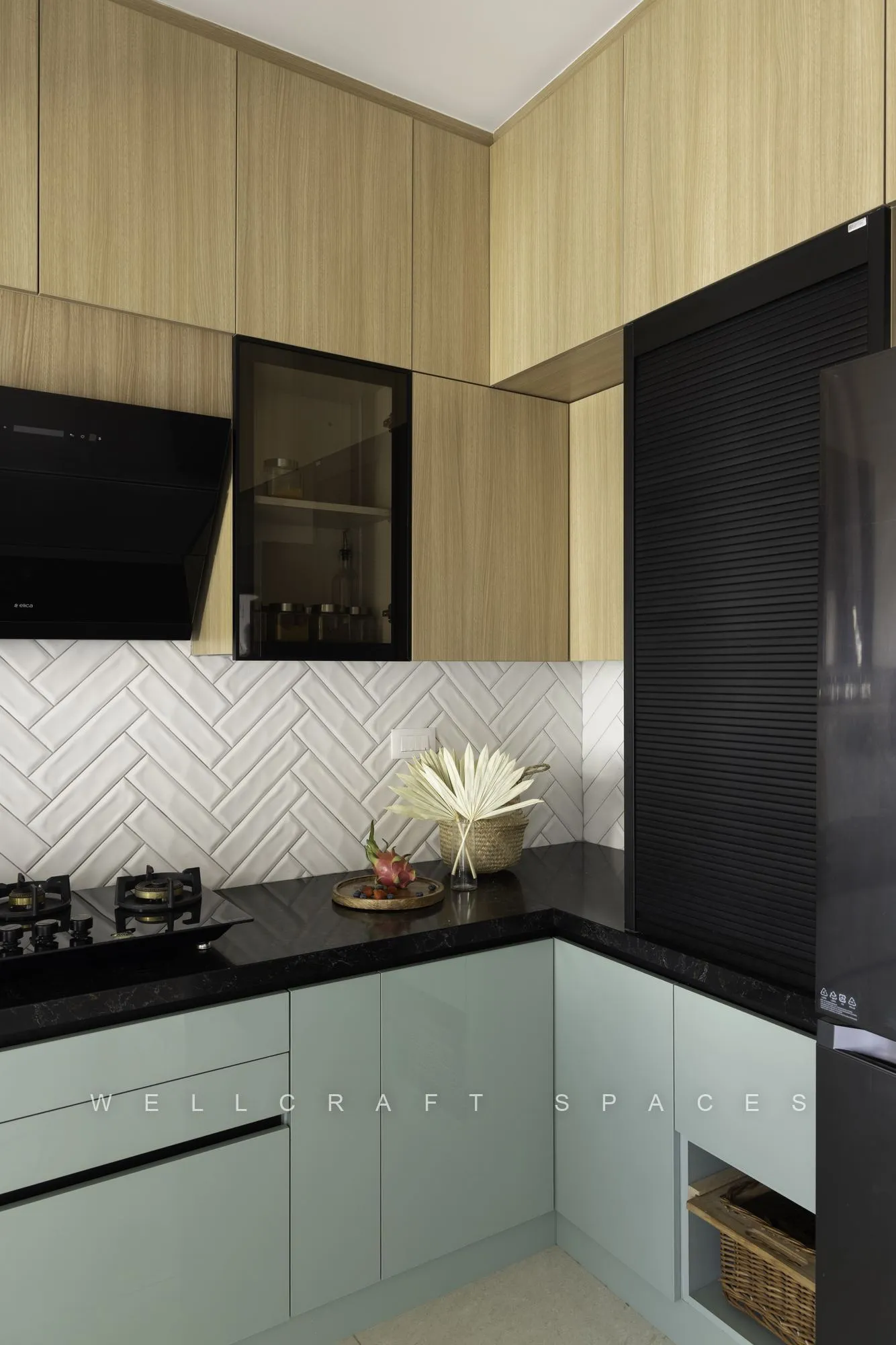L-shaped kitchen run in mint and oak with a built-in oven, dark tall unit and herringbone tiling behind the counter.