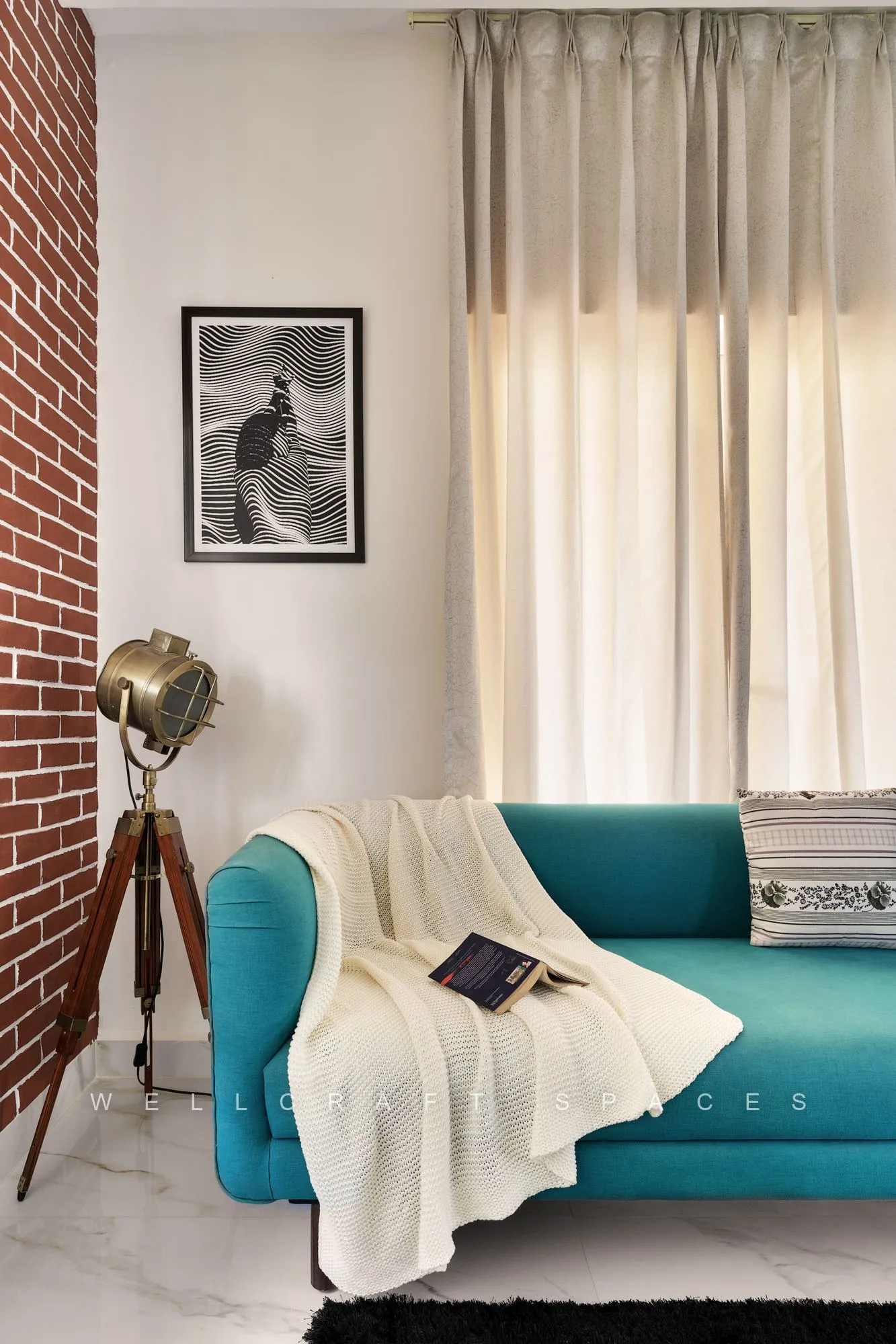 Teal three-seater with kilim cushions and a cream throw beside a brass tripod floor lamp, framed by a brick pier and sheer sage curtains.