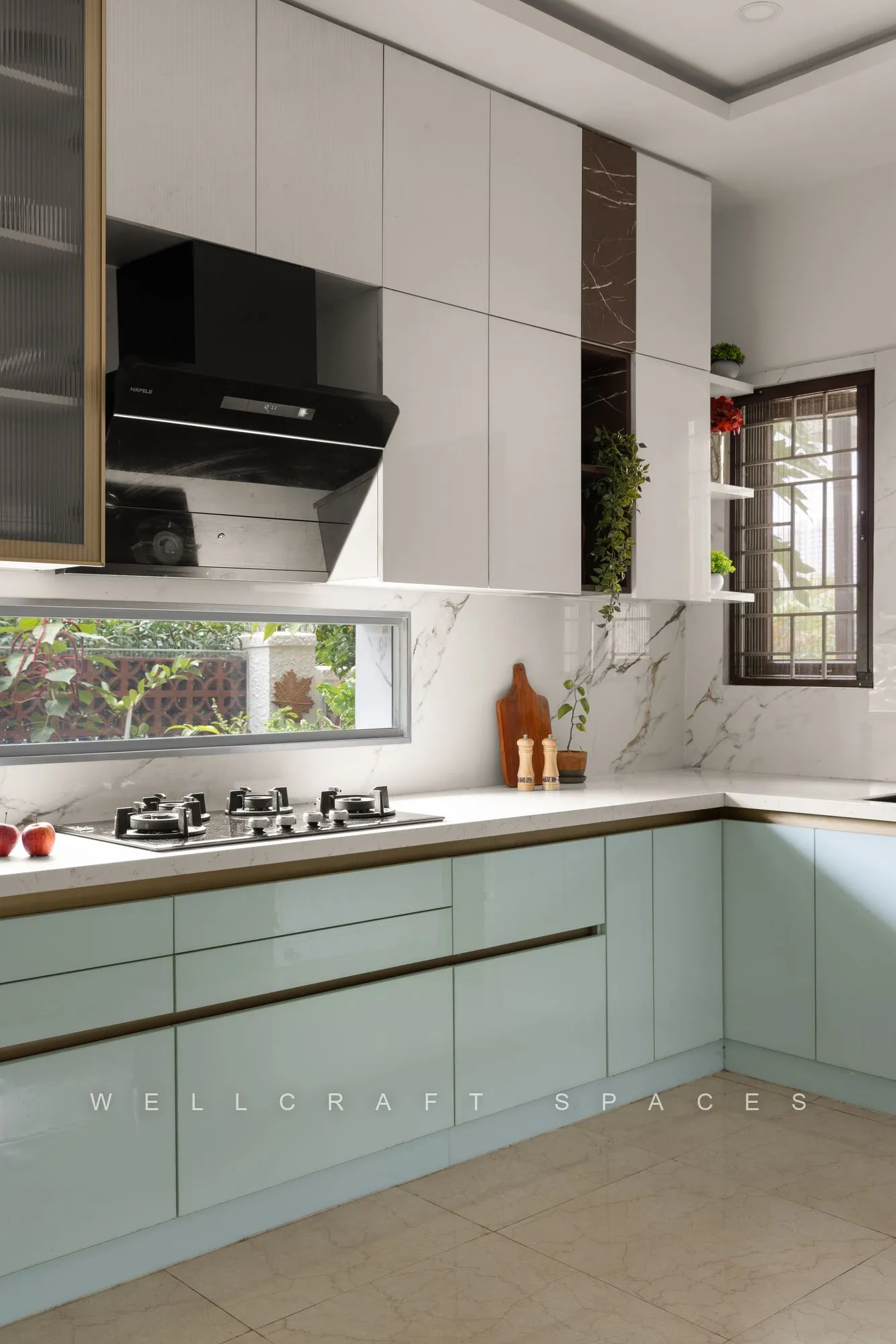 Kitchen in pale mint gloss cabinetry with a white stone counter, marble-look backsplash, black chimney hood and a window over the hob.