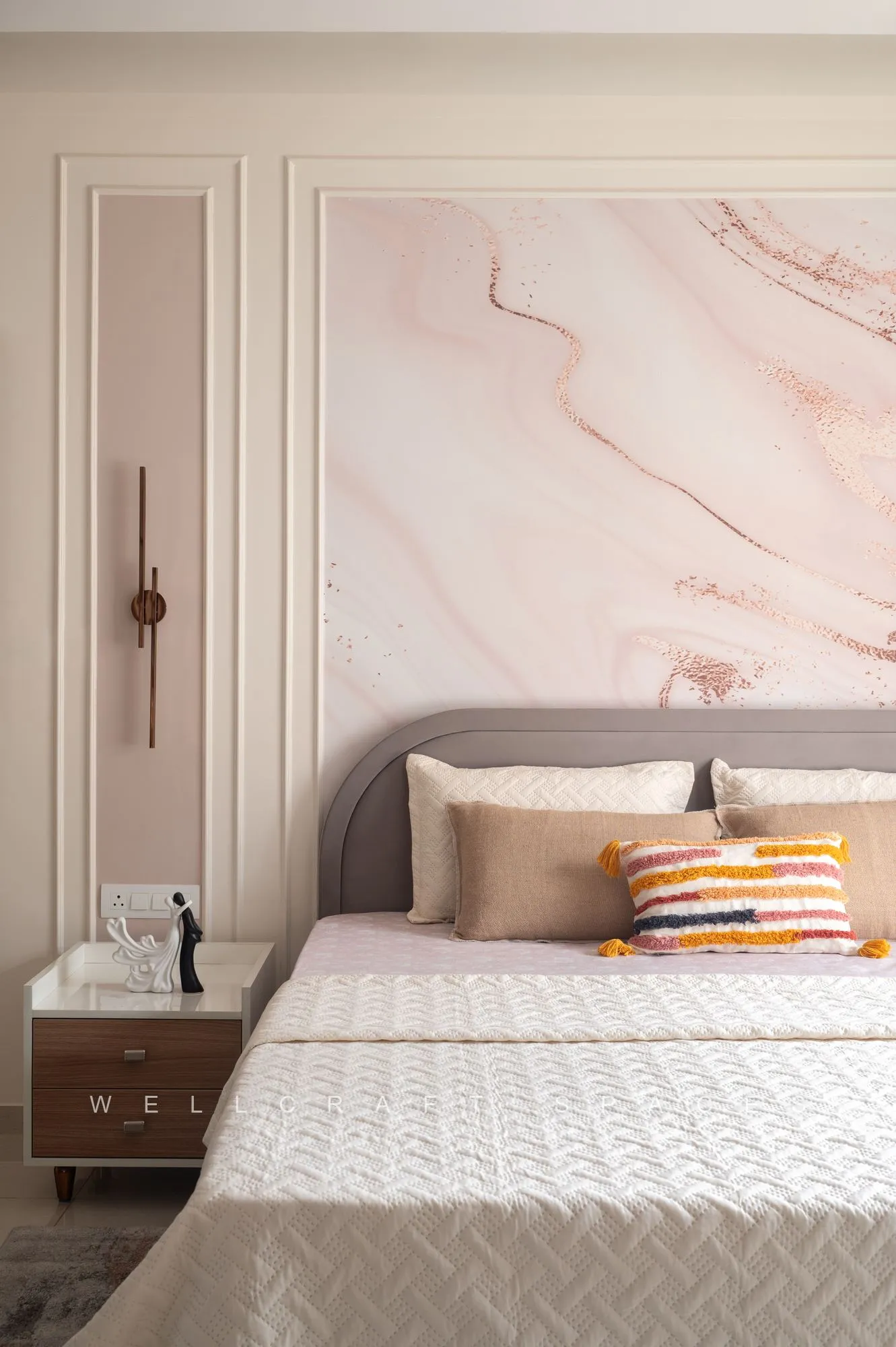 Primary bedroom with a pink marble-effect panelled headboard wall, upholstered bed in white quilting and a walnut bedside table.