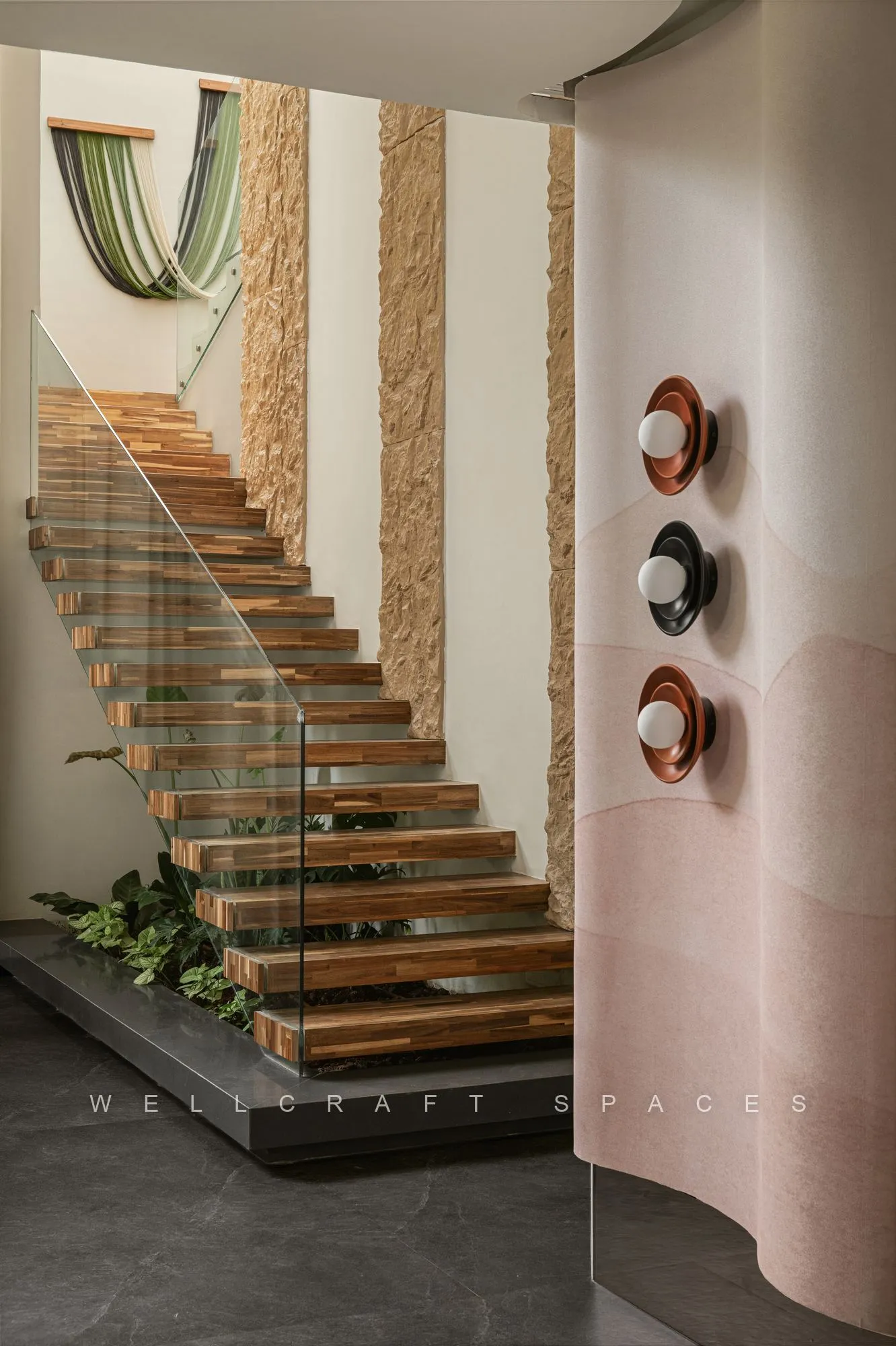 Floating timber staircase against a blush plaster wall hung with circular ceramic discs, with trailing plants at its base.