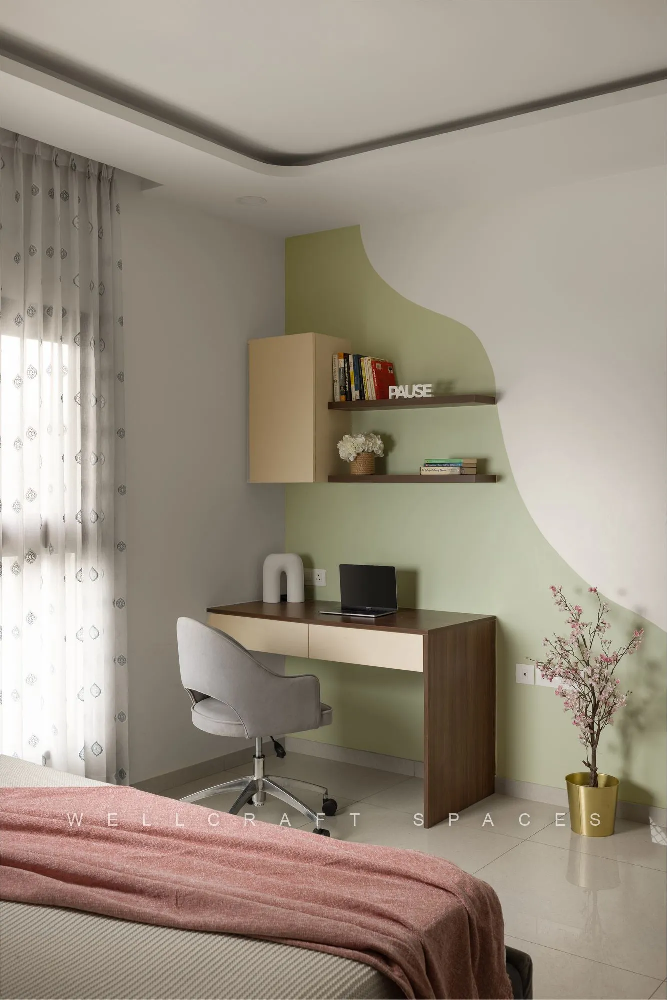 Bedroom study corner with a walnut desk, white swivel chair and open shelves set against a sage green curved wall panel.