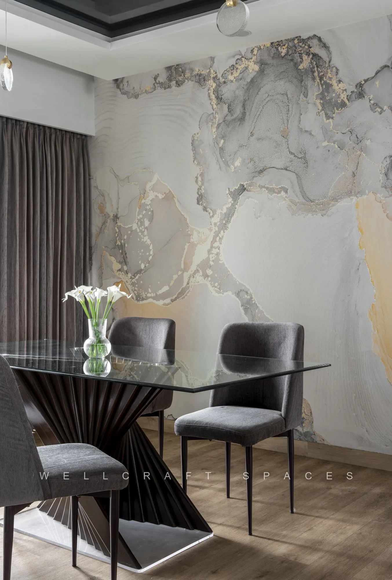 Dining table with a fluted timber pedestal base and grey upholstered chairs, set against a dramatic grey and gold marble-effect mural wall.