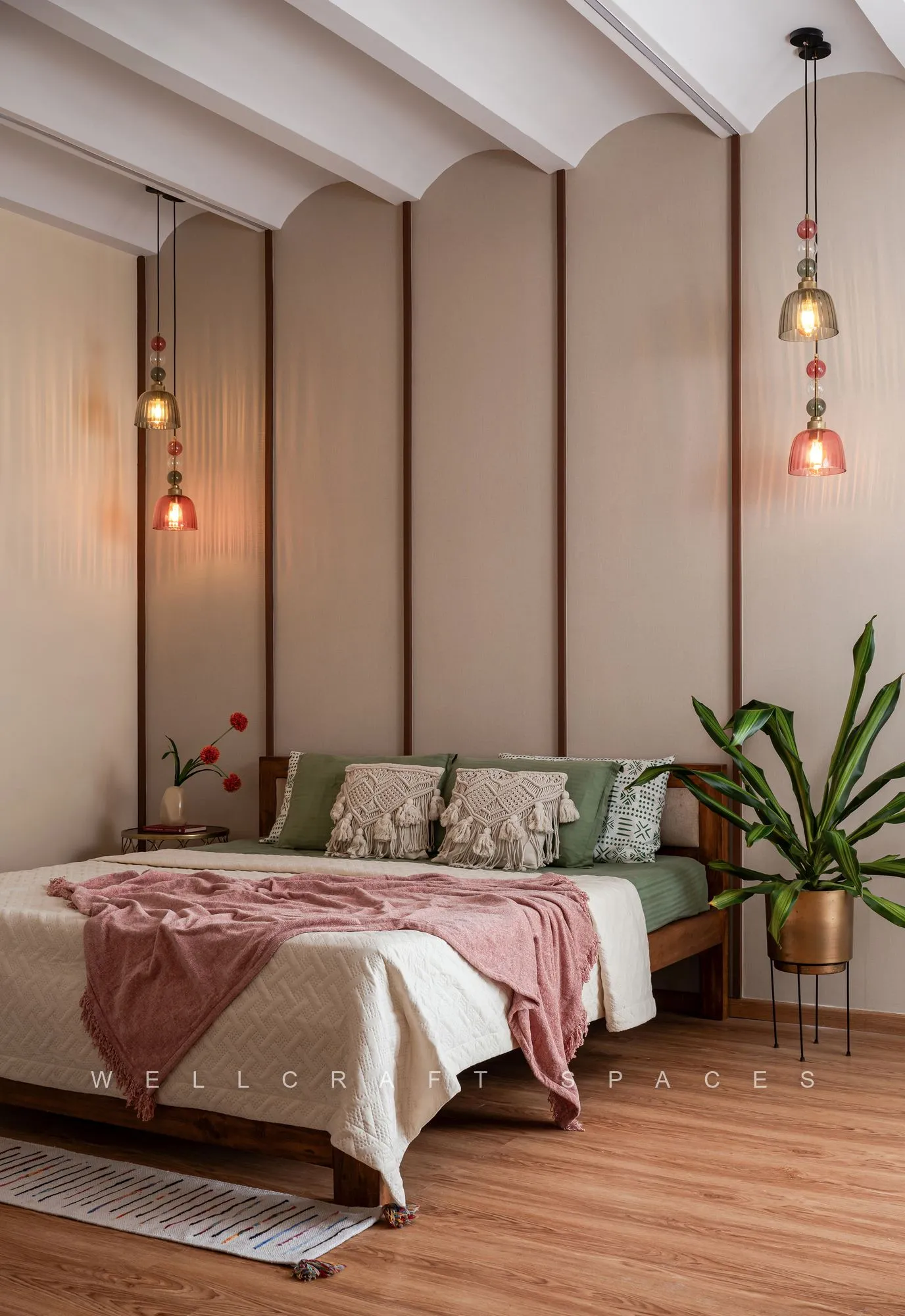 Master bedroom with a blush fluted headboard wall rising to a vaulted beamed ceiling, layered pink and cream bedding and amber glass pendants either side.