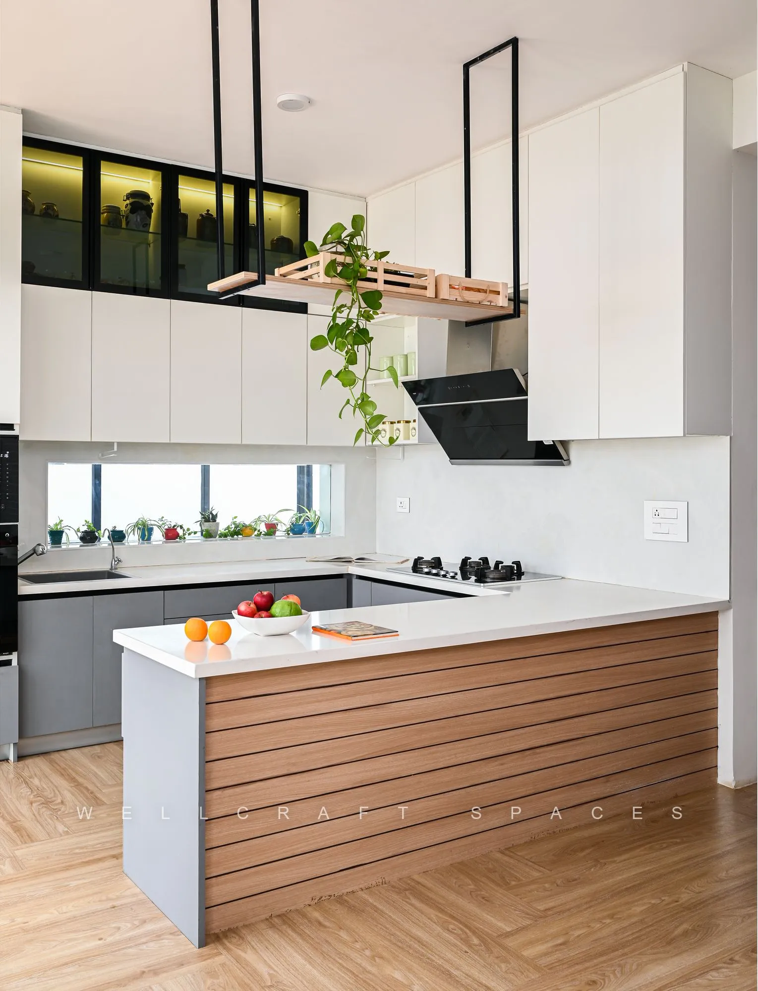 Open kitchen with a fluted walnut island, grey base cabinets, white quartz counters and black-framed glass upper shelving over herringbone oak flooring.