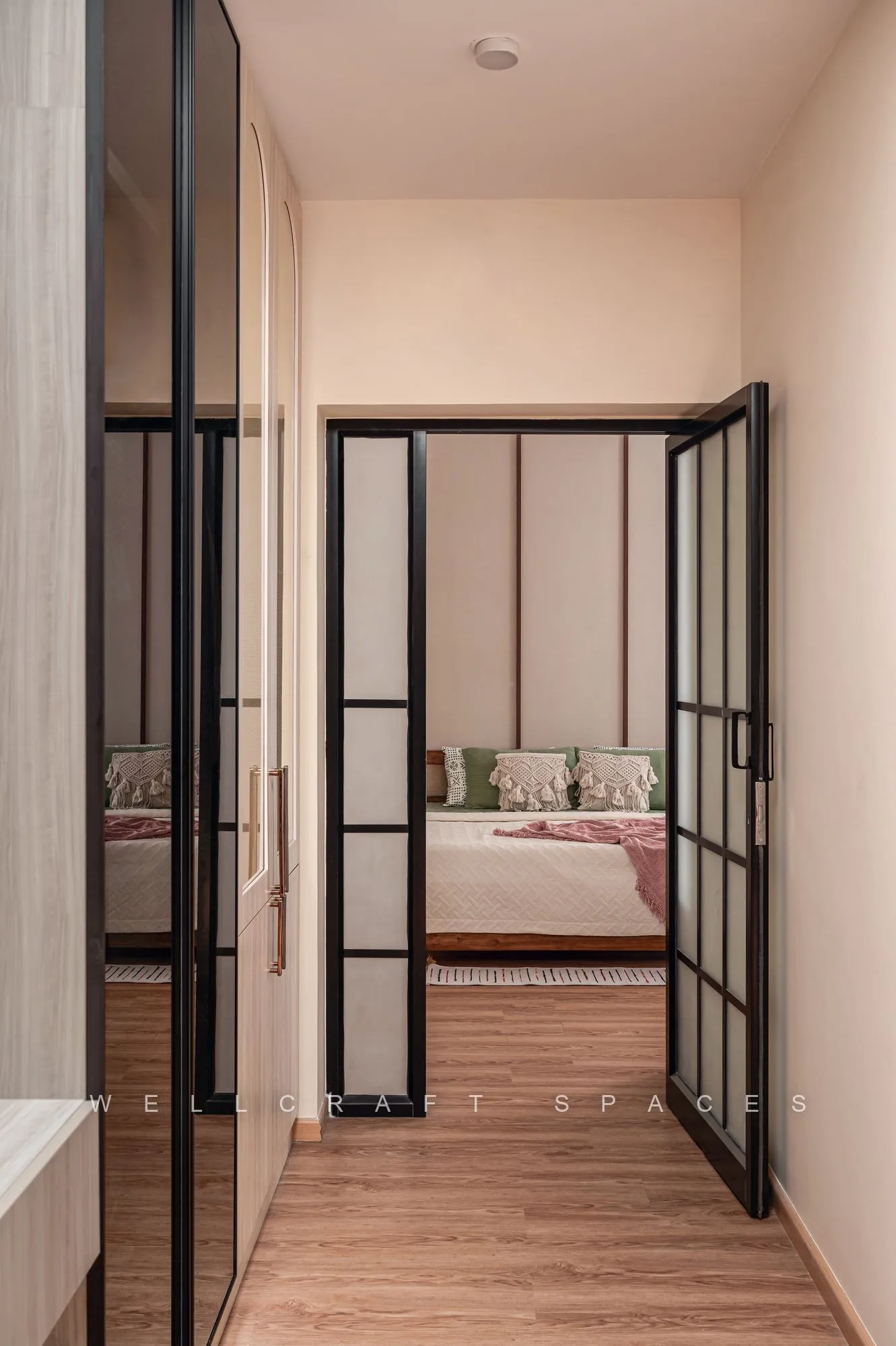 Black-framed glass doors leading from the walk-in wardrobe passage into the bedroom, over warm oak flooring.