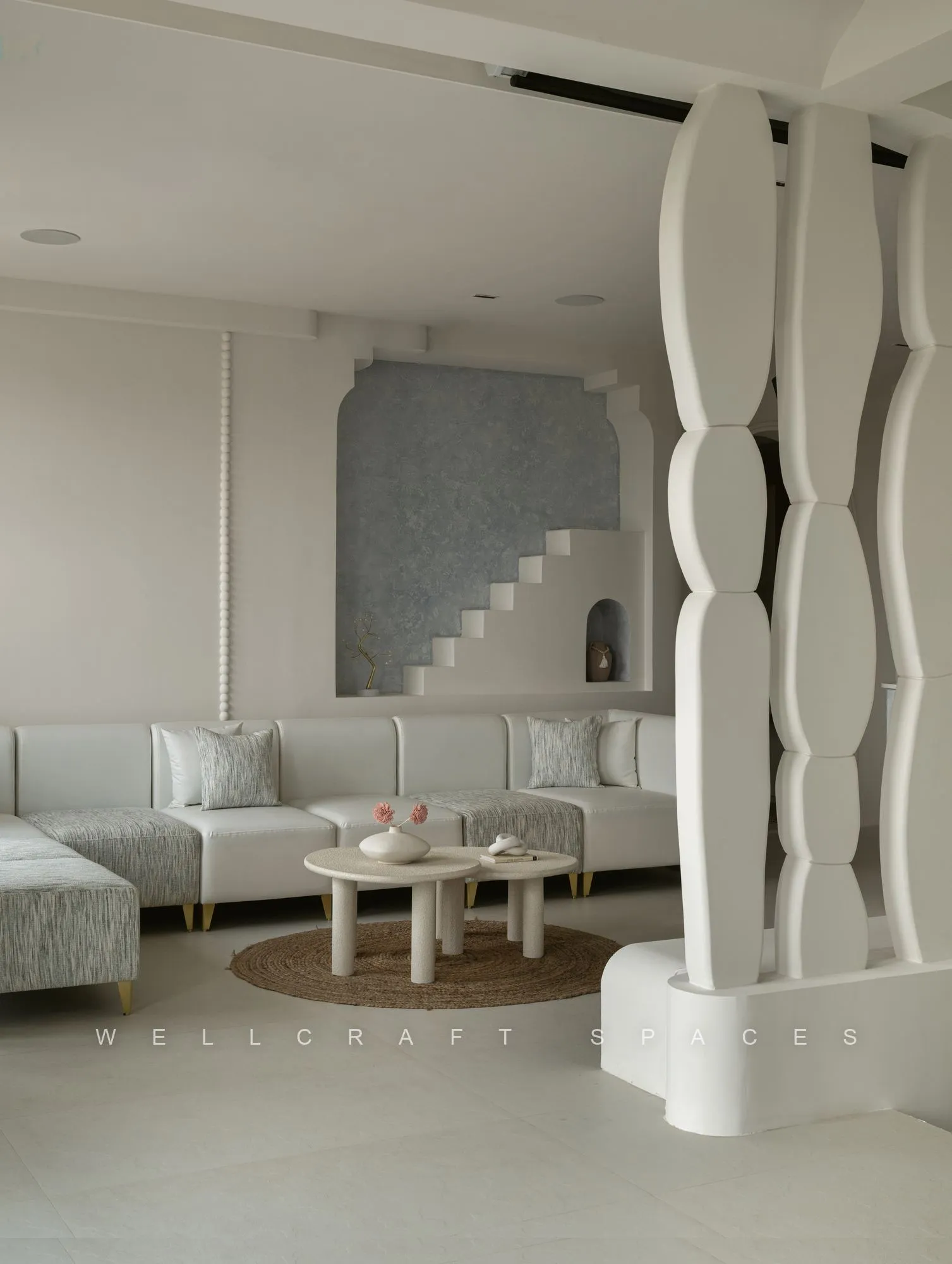 Upper lounge in soft white with sculptural curved columns, low bouclé seating, round side tables and a pale terrazzo floor.
