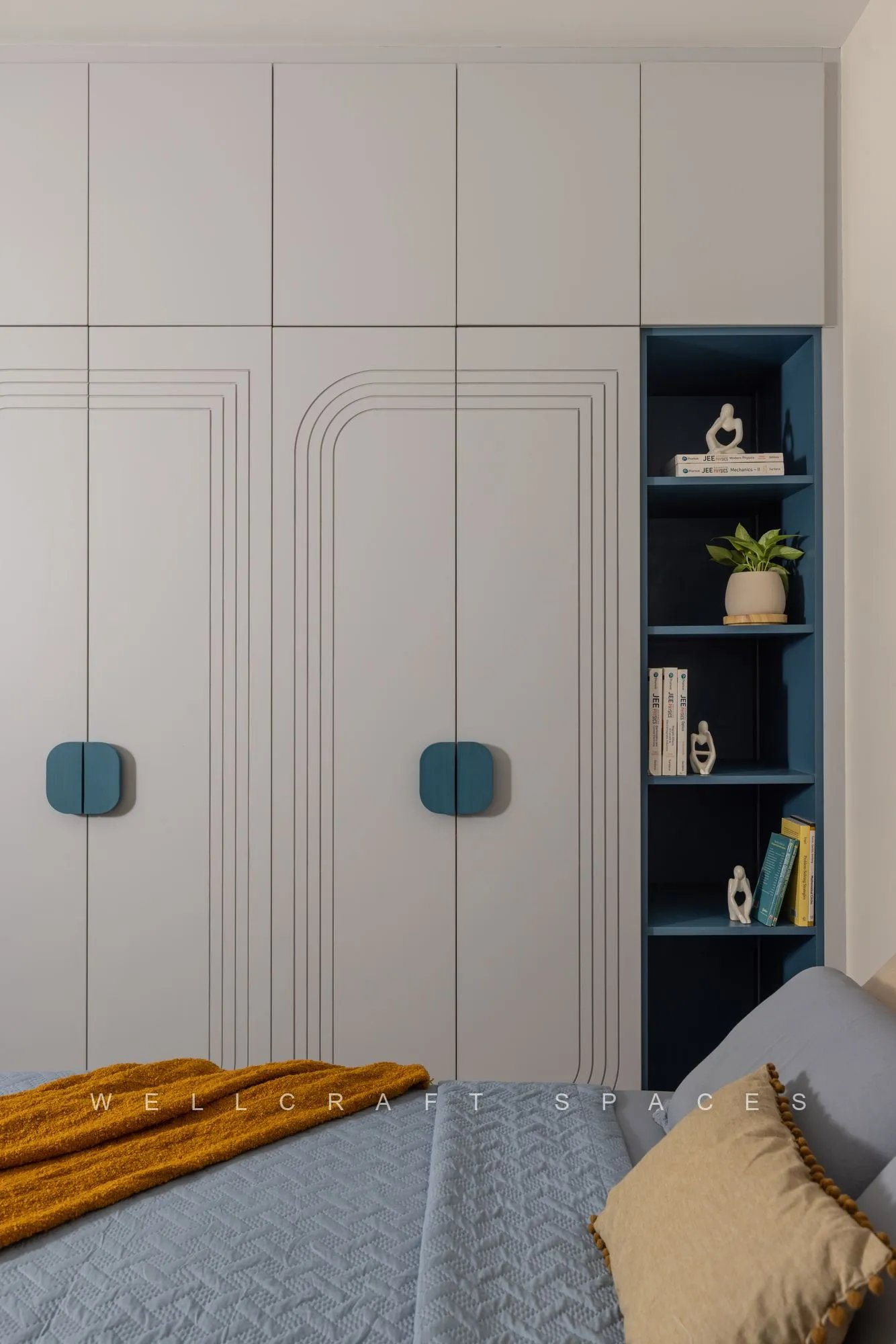 Full-height white wardrobe with routed panel detail and teal handles, next to an open peacock-blue display shelf.