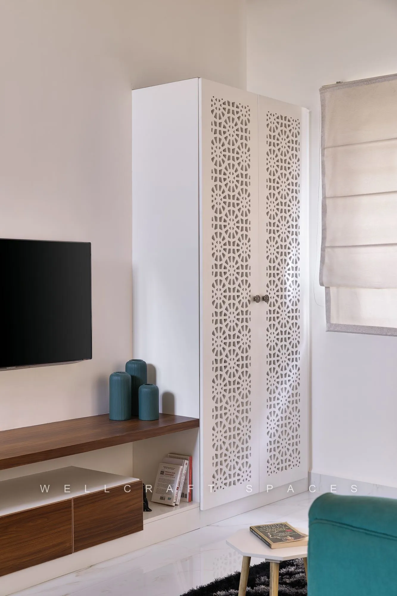 Media wall in the lounge with a wall-mounted television, a walnut floating console, a slim jali-patterned tall cabinet and pale ceramic vases.
