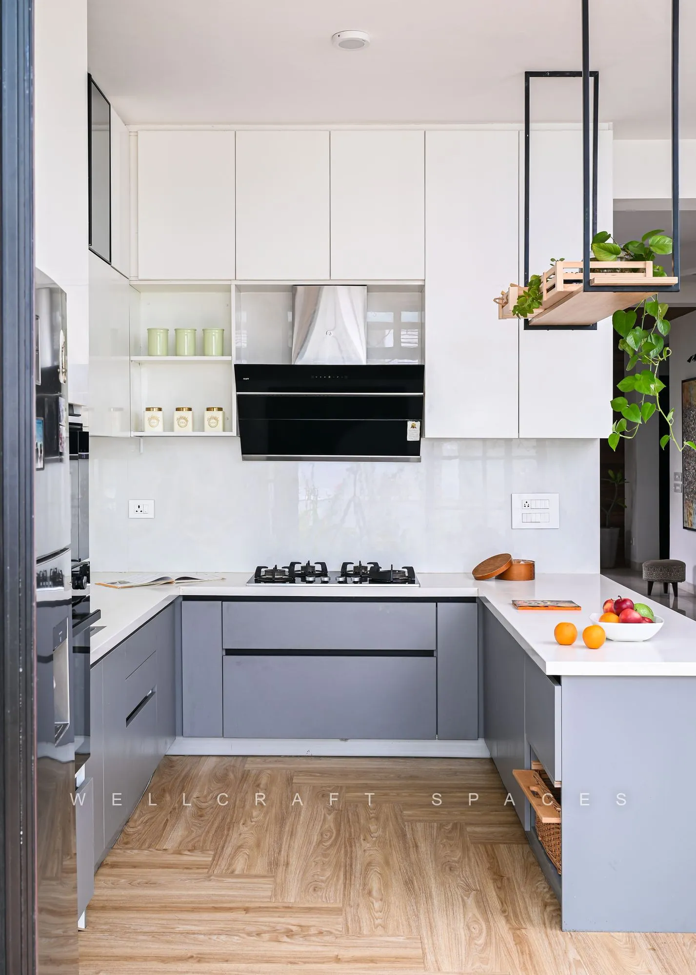Working leg of the kitchen in dove-grey shutters and white counters, with a black chimney hood, glass wall cabinets and a strip of window above the backsplash.