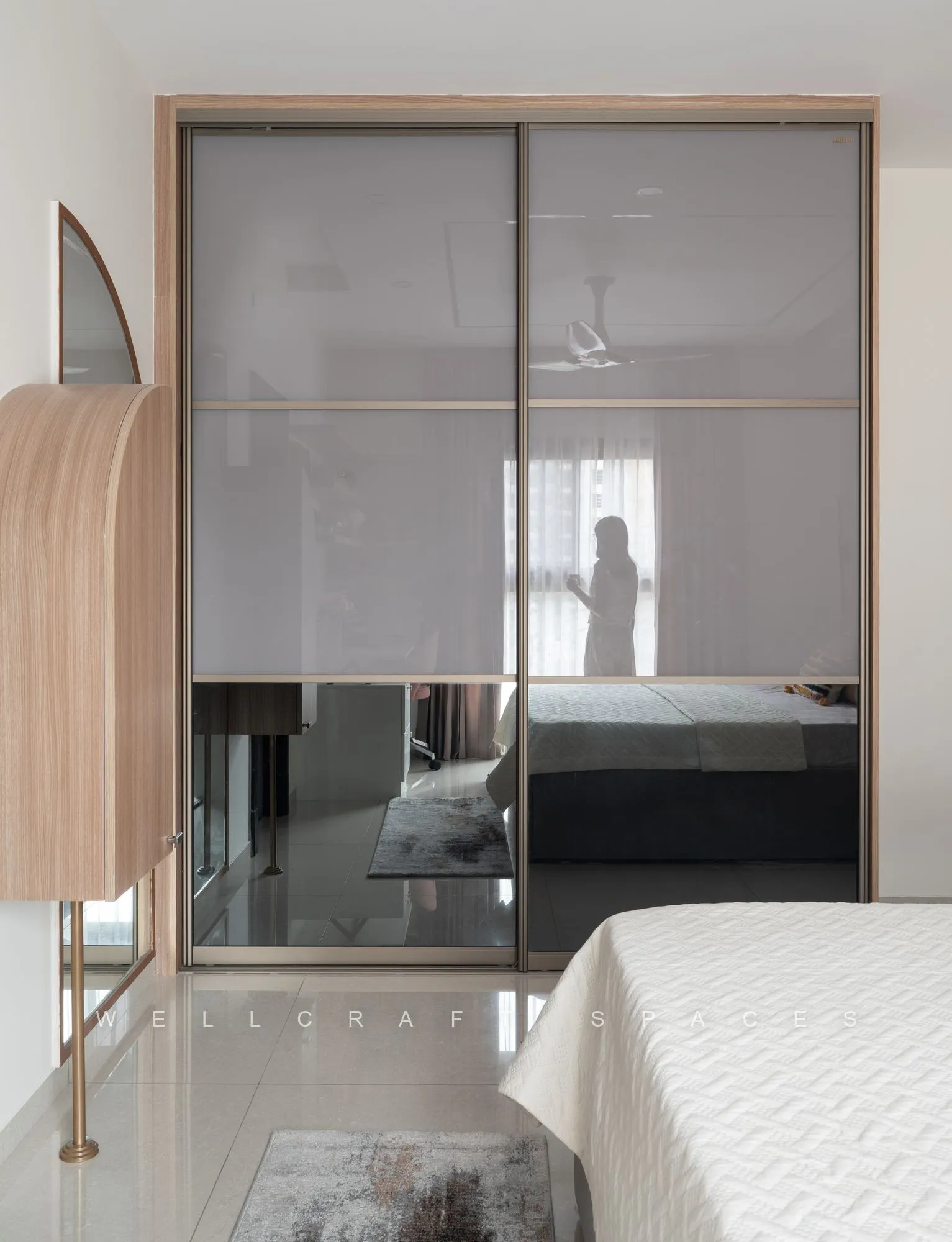 Sliding mirrored wardrobe in light oak framing reflecting the bed, with a tall arched full-length mirror alongside.
