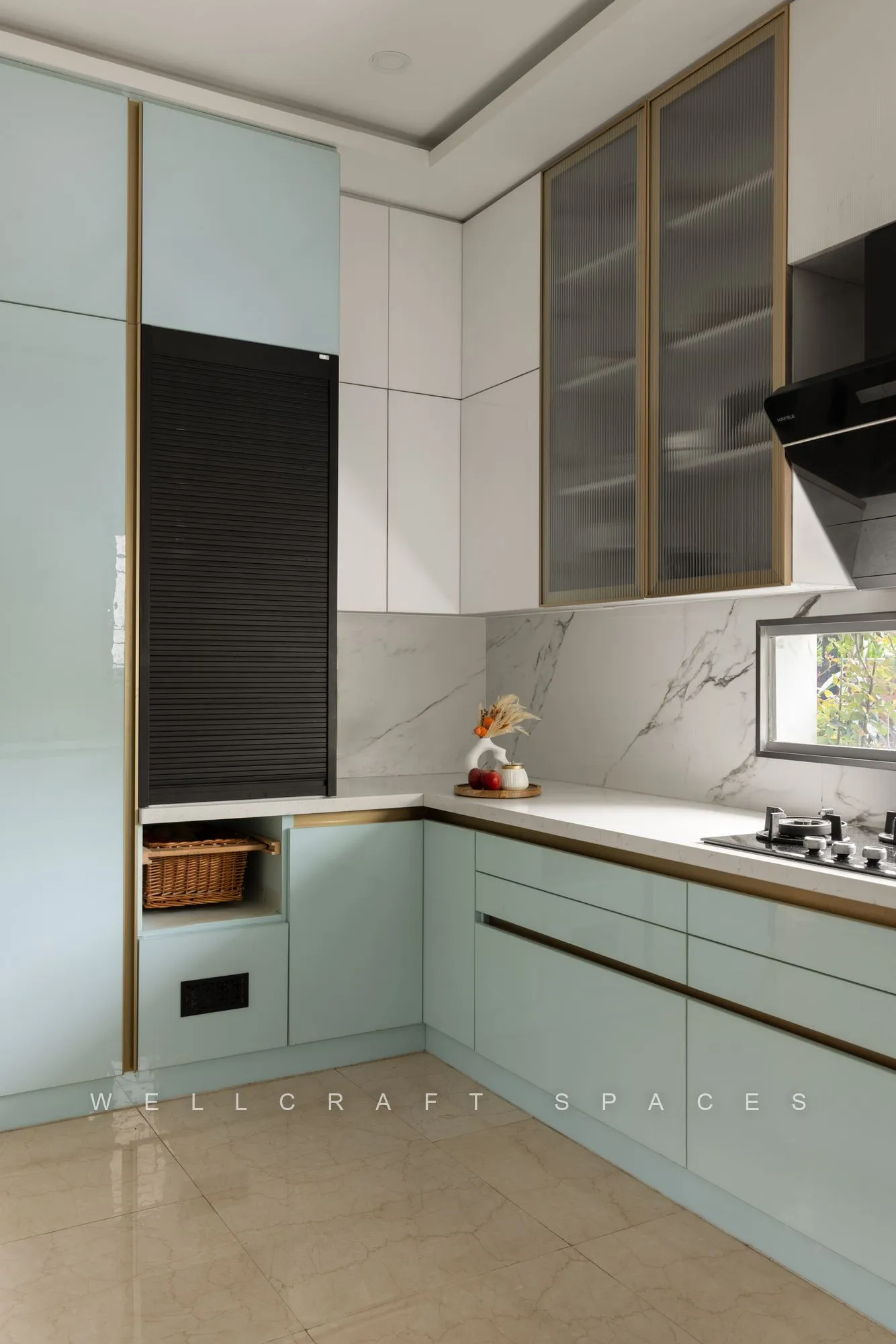 Corner view of the mint kitchen showing the tall appliance column, glass-fronted uppers with brass trim and continuous under-cabinet lighting.
