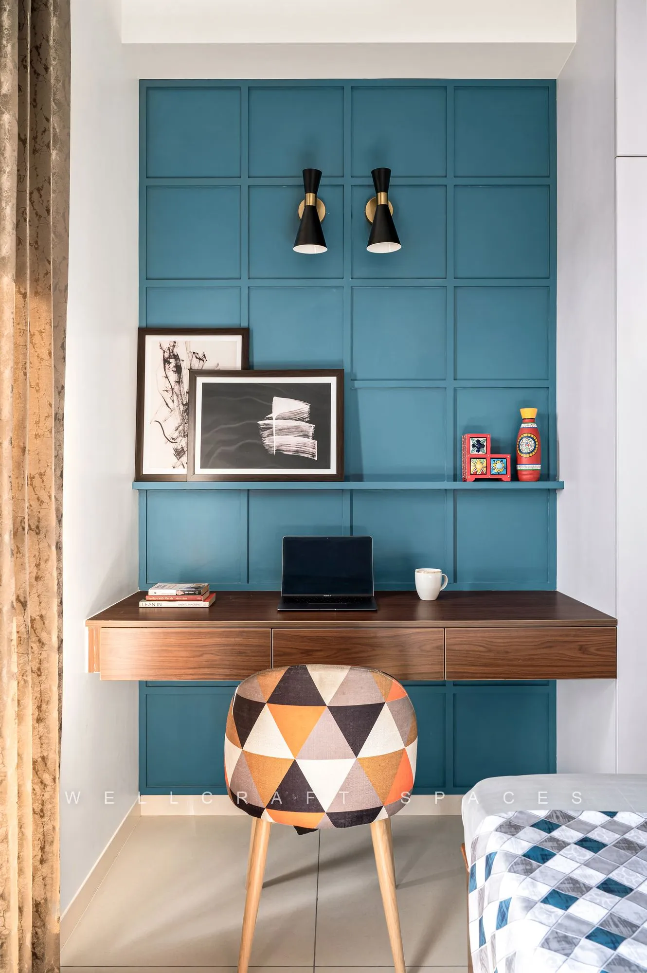 Floating walnut desk under a teal panelled wall with black cone spotlights, a geometric-print chair and framed monochrome prints.