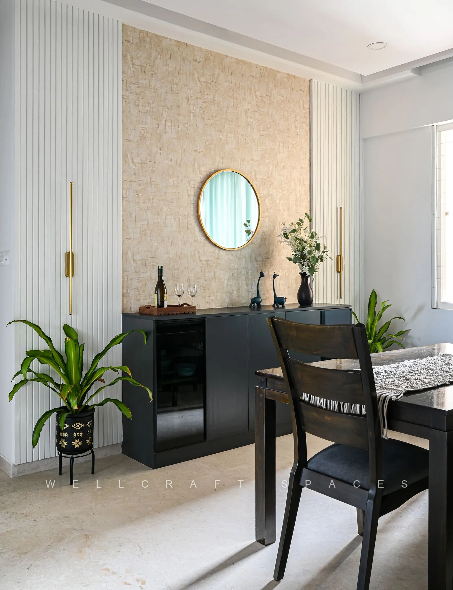 Dining corner with a black-framed glass table and cane-back chairs, a round mirror on textured wallpaper and a slim bar unit alongside.