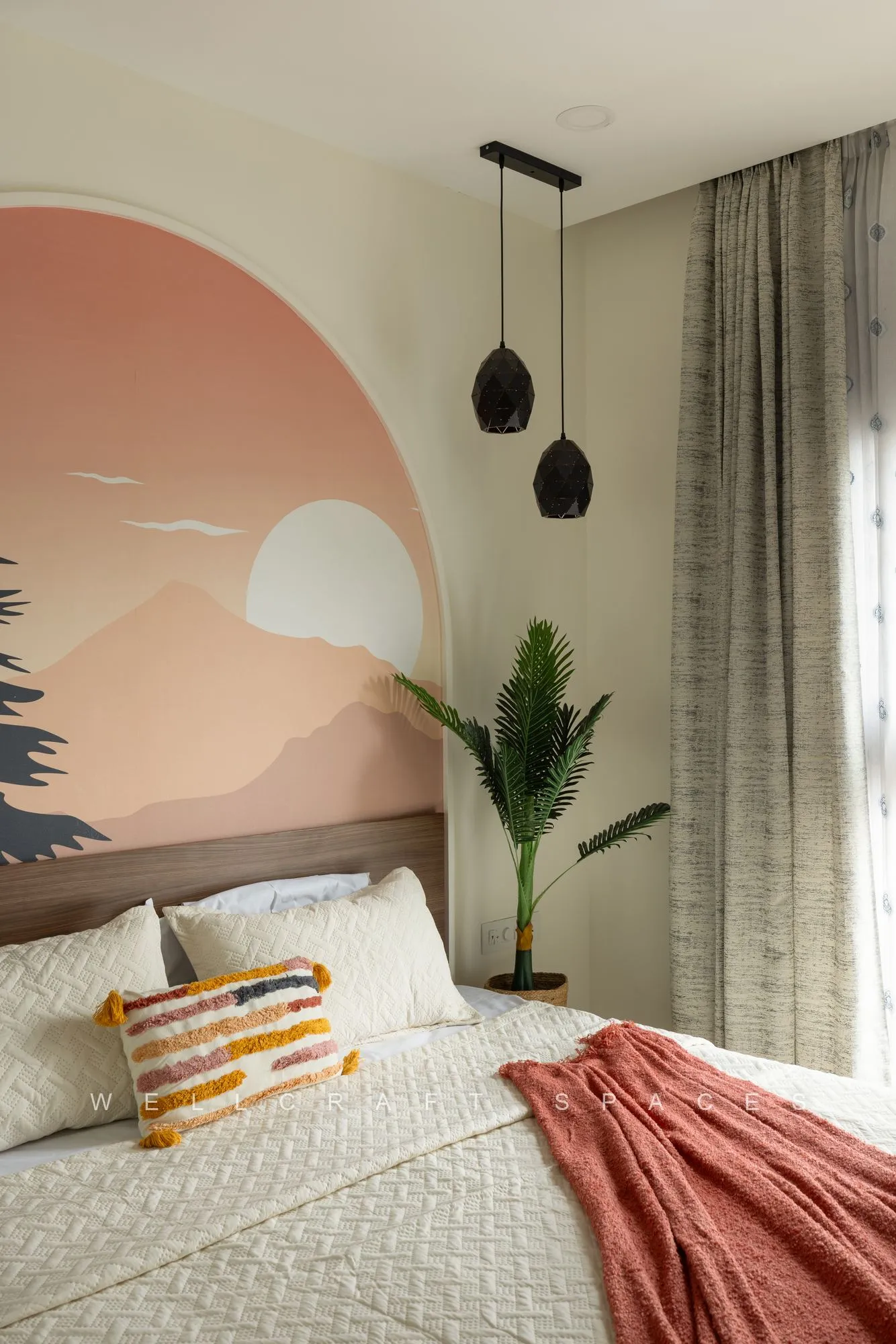 Guest bedroom with a painted sunrise and pine-tree mural arch behind the bed, rust throw, striped cushions and a black pendant light.