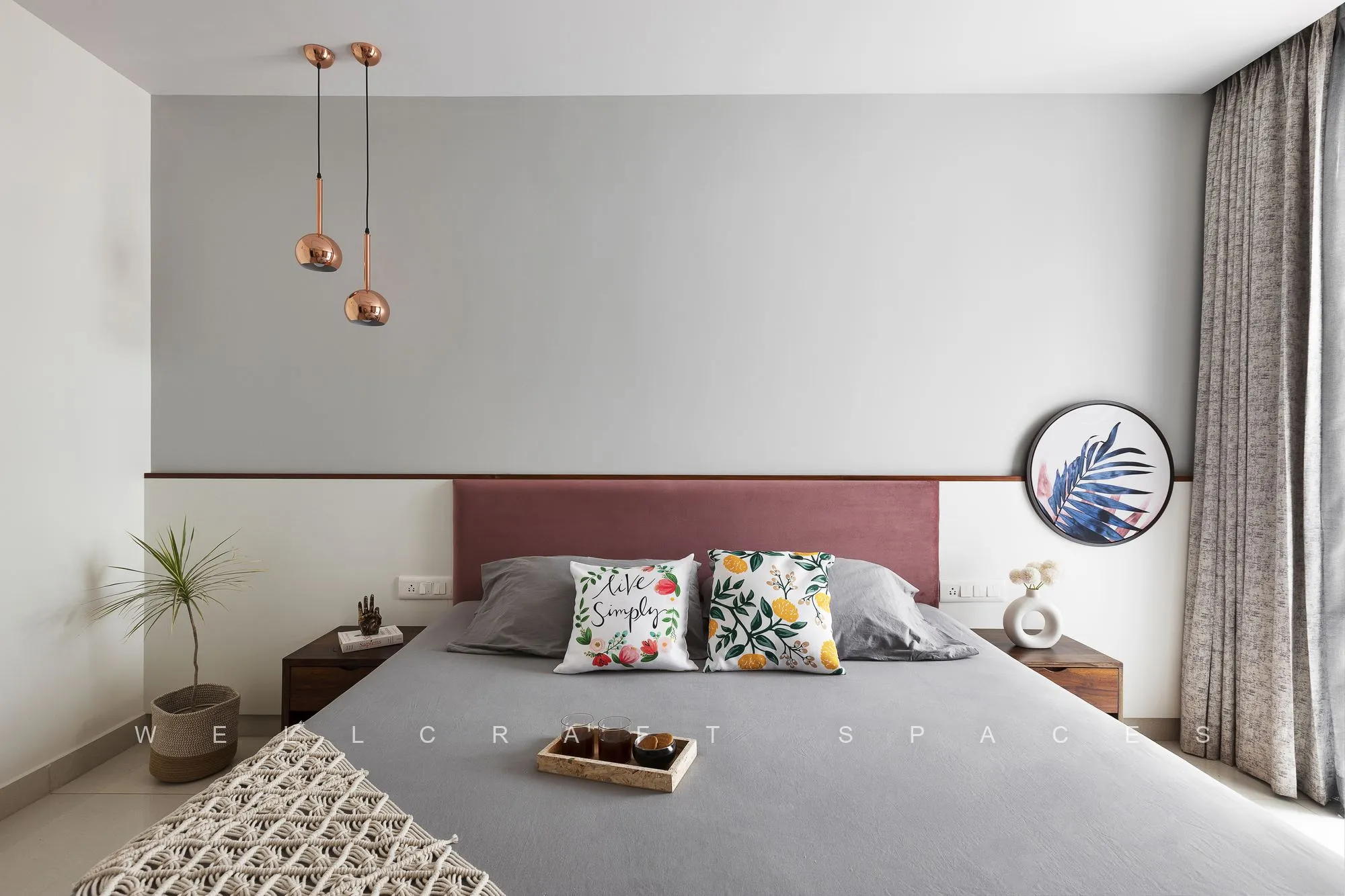 Master bedroom with a maroon upholstered headboard panel, teak bed frame, grey bedding and twin copper pendants at the bedside.