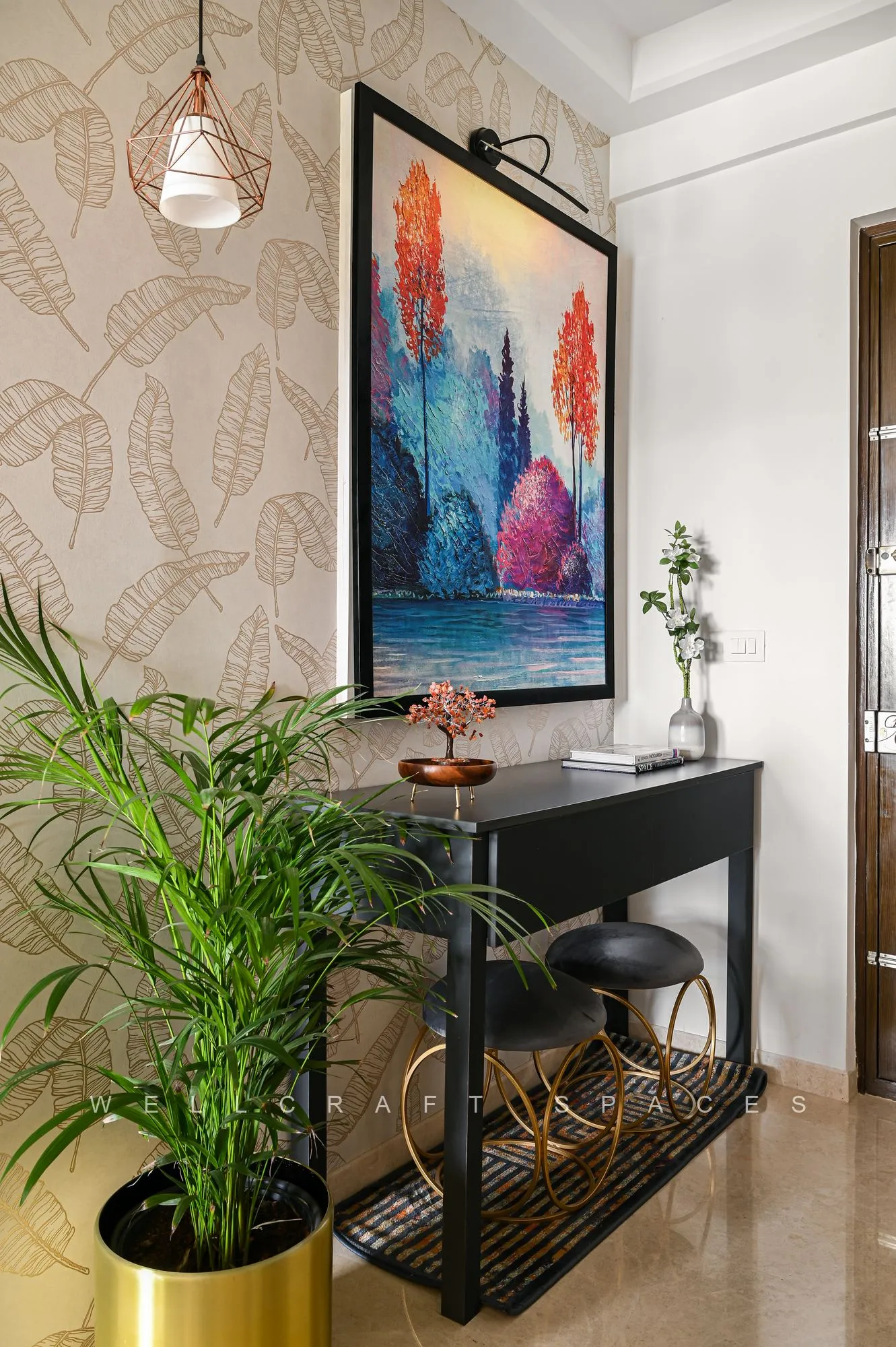 Entry vignette with a slim black console on brass legs, a colourful abstract painting above and a tall palm in a brass planter.
