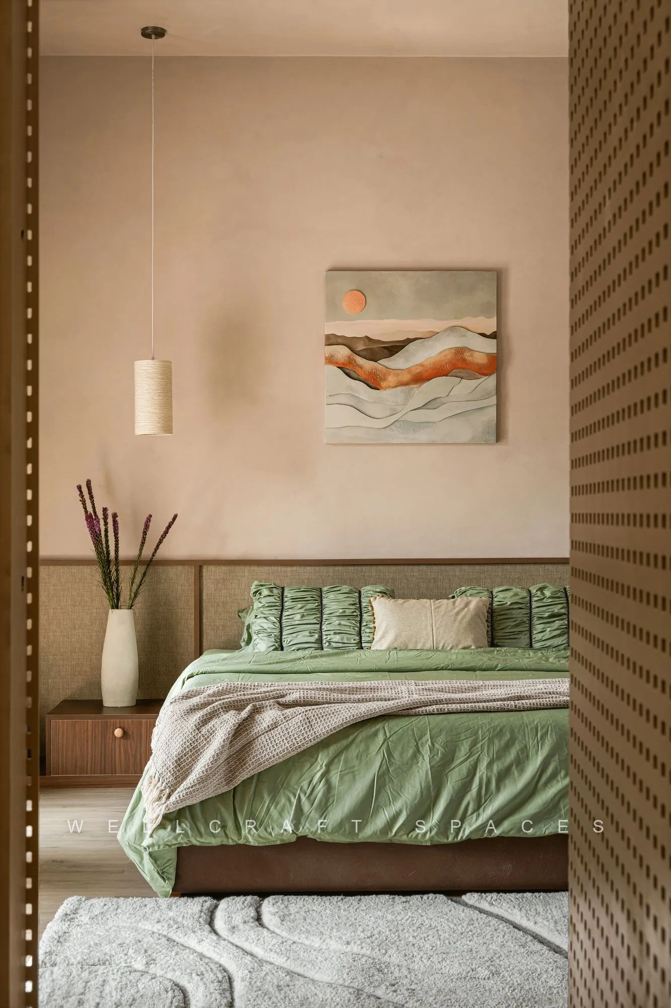 Bedroom with a sage green bed set into a fluted timber headboard frame, a warm abstract artwork above and slim wall sconces.