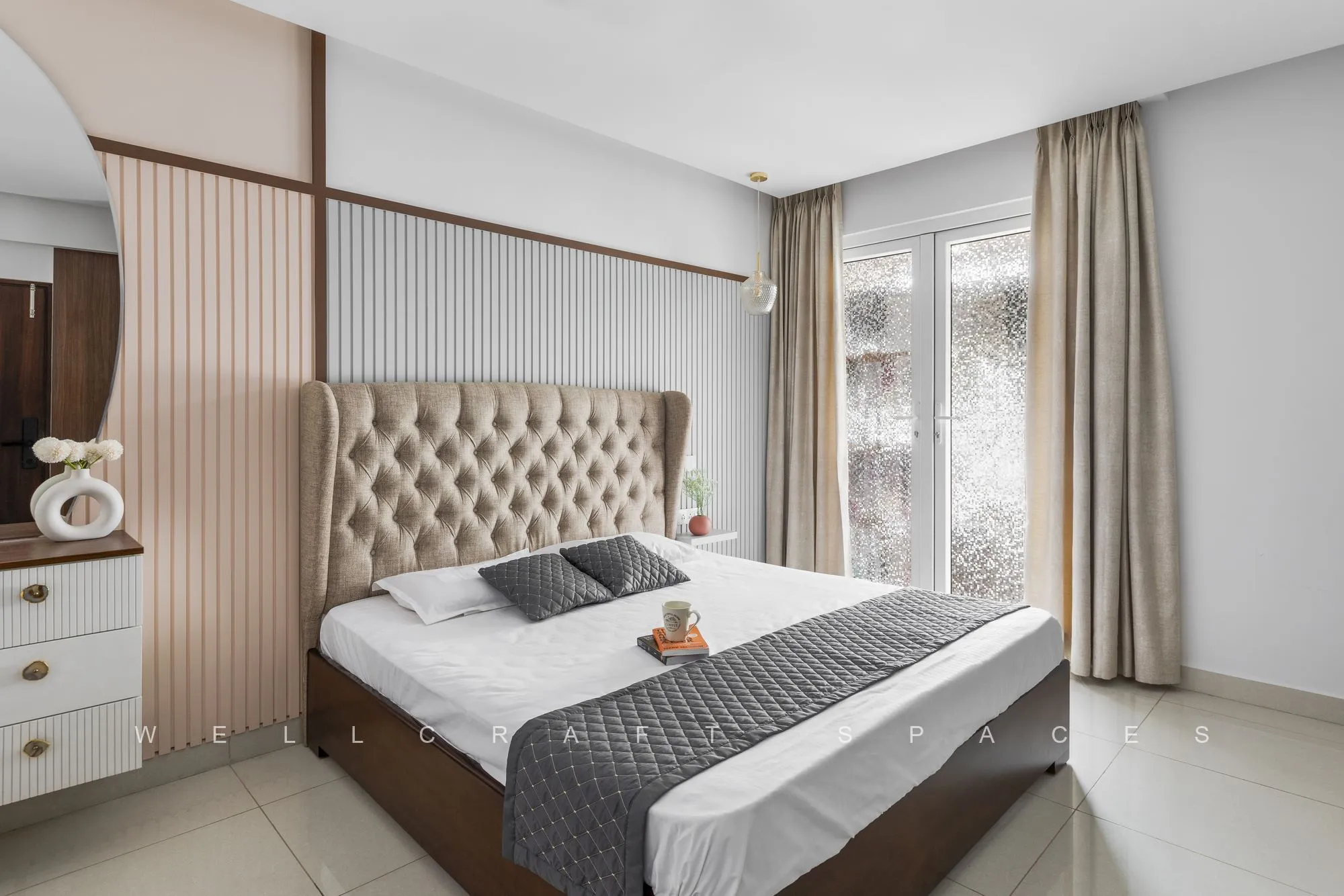 Master bedroom with a tall tufted beige headboard, charcoal and white bedding, fluted wall panelling and sheer-curtained window.