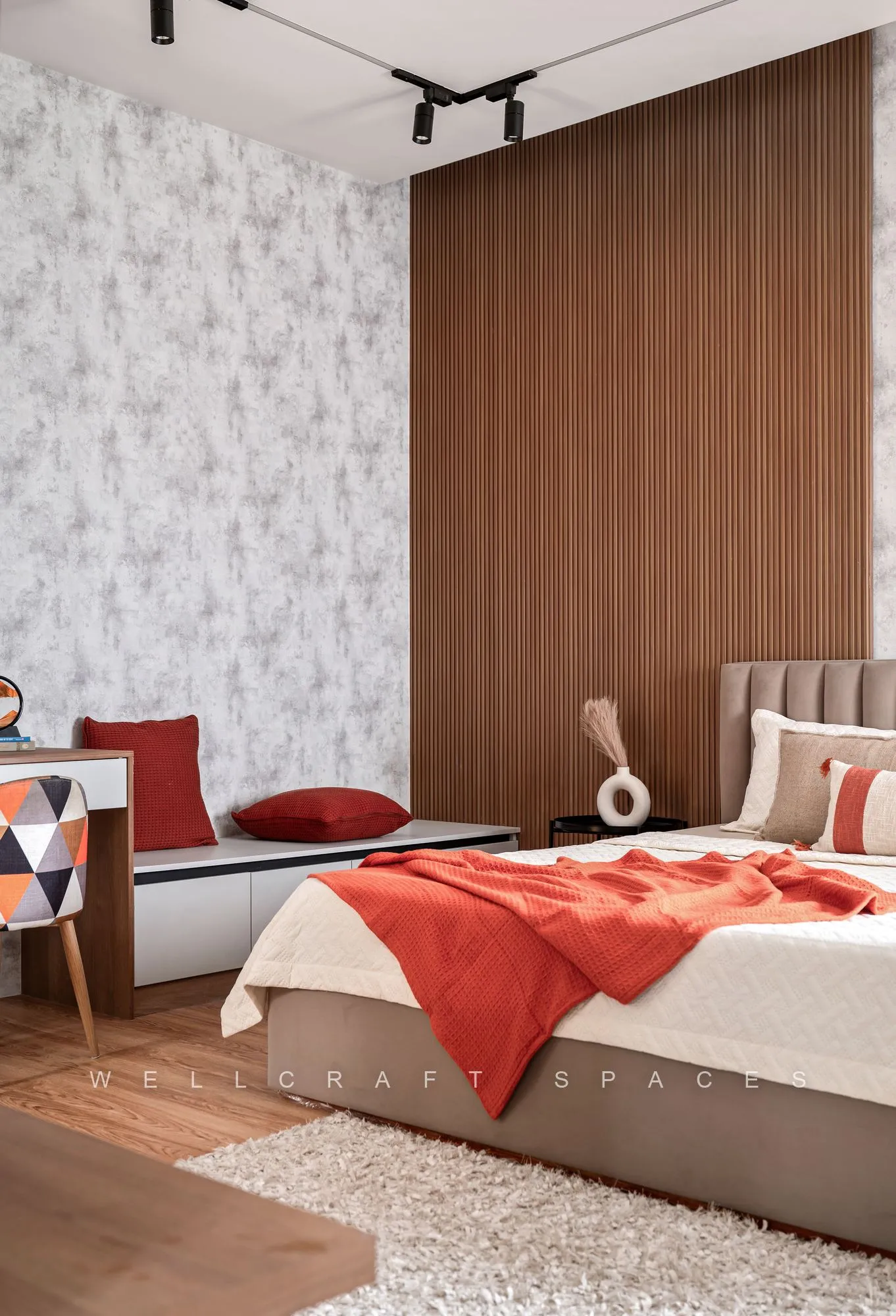 Bedroom with a warm walnut slatted wall, mottled grey wallpaper, a beige upholstered bed dressed in rust and cream, and a low window bench.