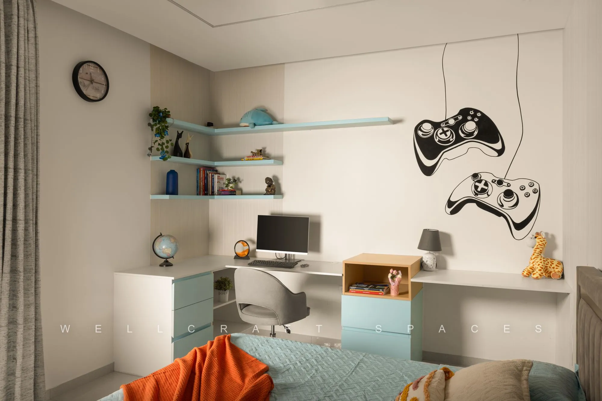 Wider view of the kids room with game-controller wall decals, a light blue desk unit, open shelves and an orange bedspread.