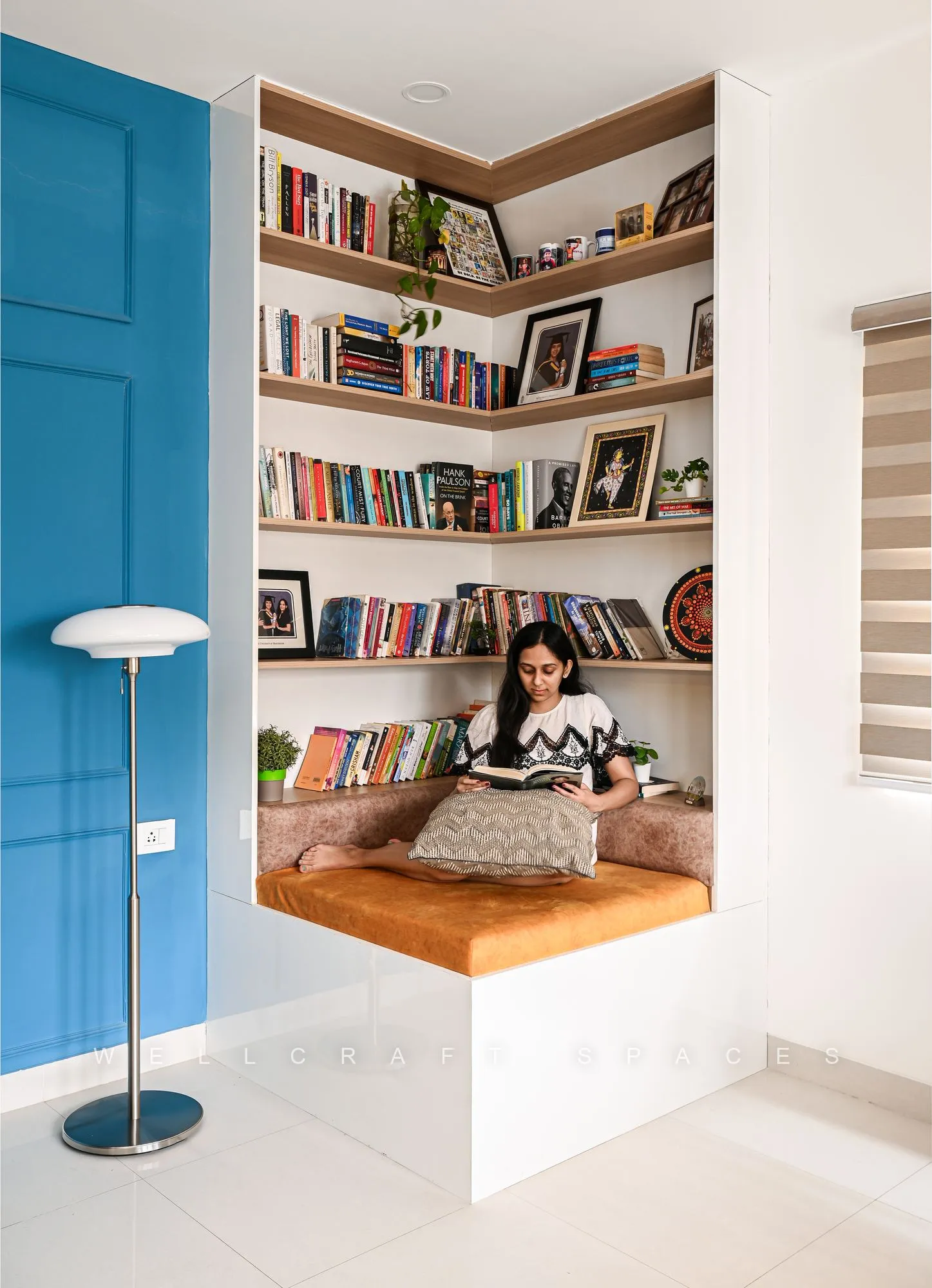 Reading nook detail showing the cantilevered oak bench and shelves of books and framed photographs against the teal panelled wall.
