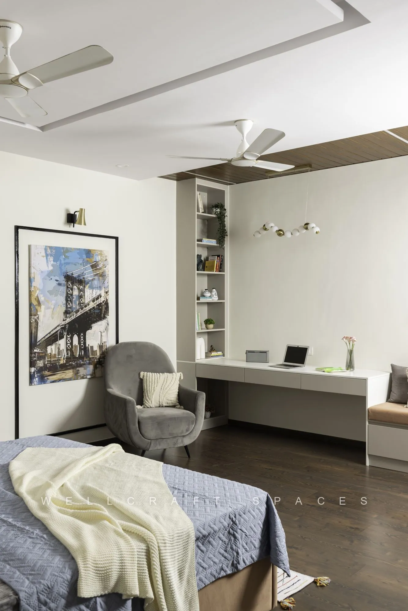 Bedroom with a built-in desk and open shelving along the window wall, a grey tub chair, framed cityscape print and a lilac and cream bed.