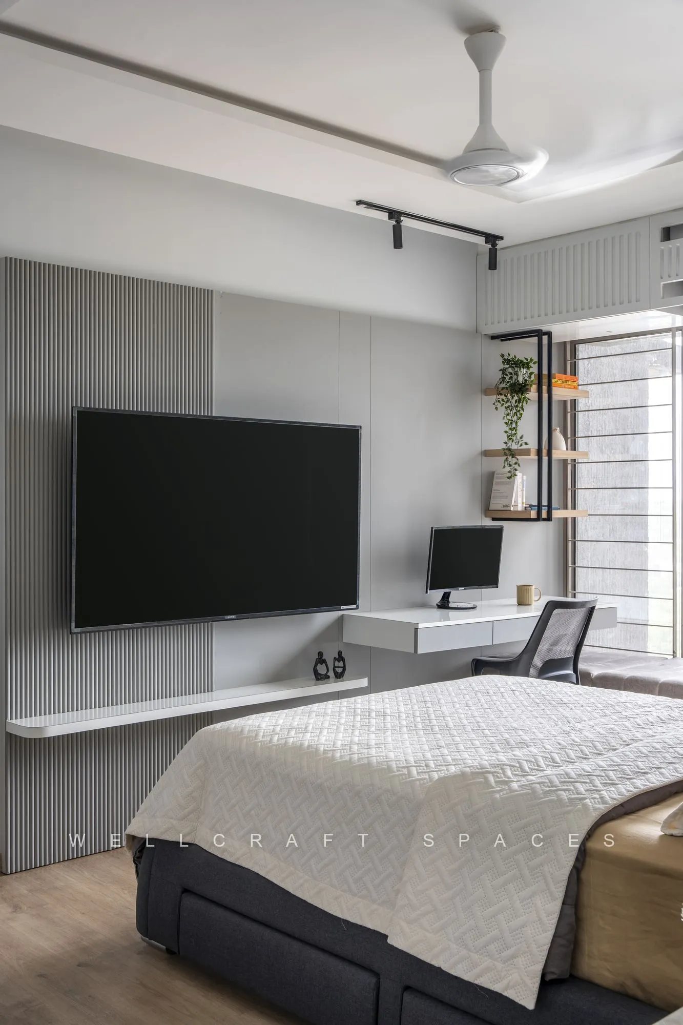 Master bedroom with a grey upholstered bed, quilted ivory bedspread, a wall-mounted television on a grey panelled wall and a slim timber shelf unit.