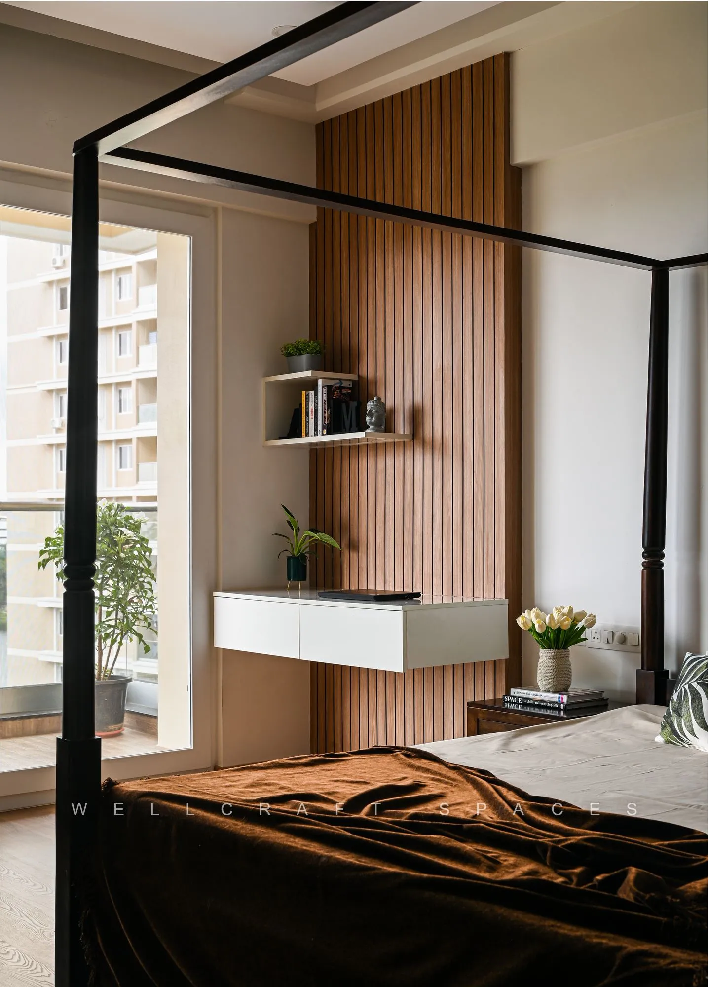 Master bedroom with a dark four-poster frame, fluted timber headboard wall, floating white bedside shelf and a brown throw.