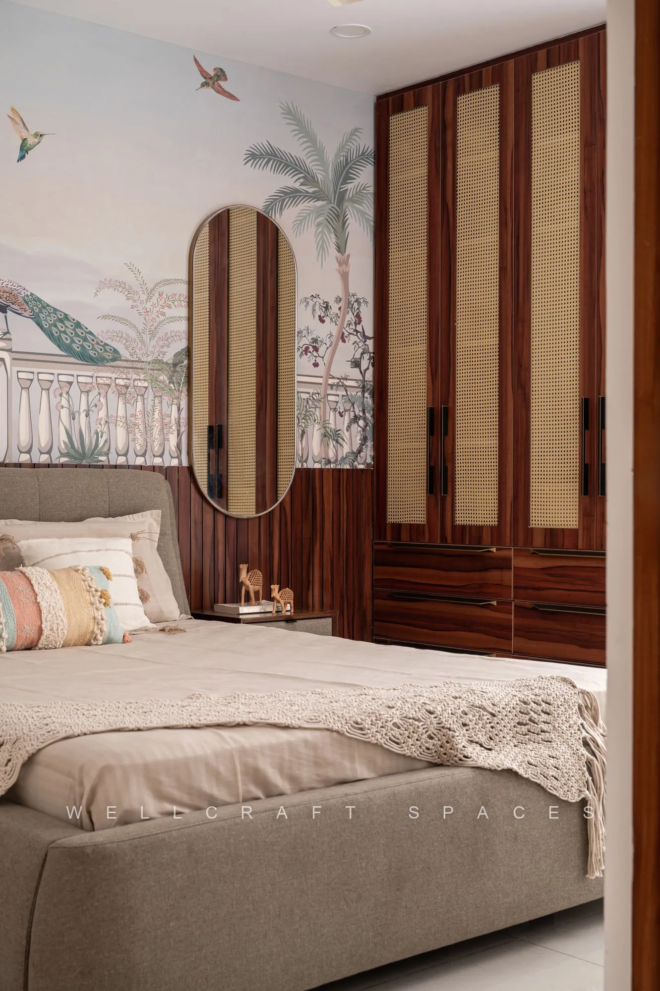 Guest bedroom with a tropical mural wall, rosewood wardrobe shutters, an arched full-length mirror and crochet-trimmed linen bedding.
