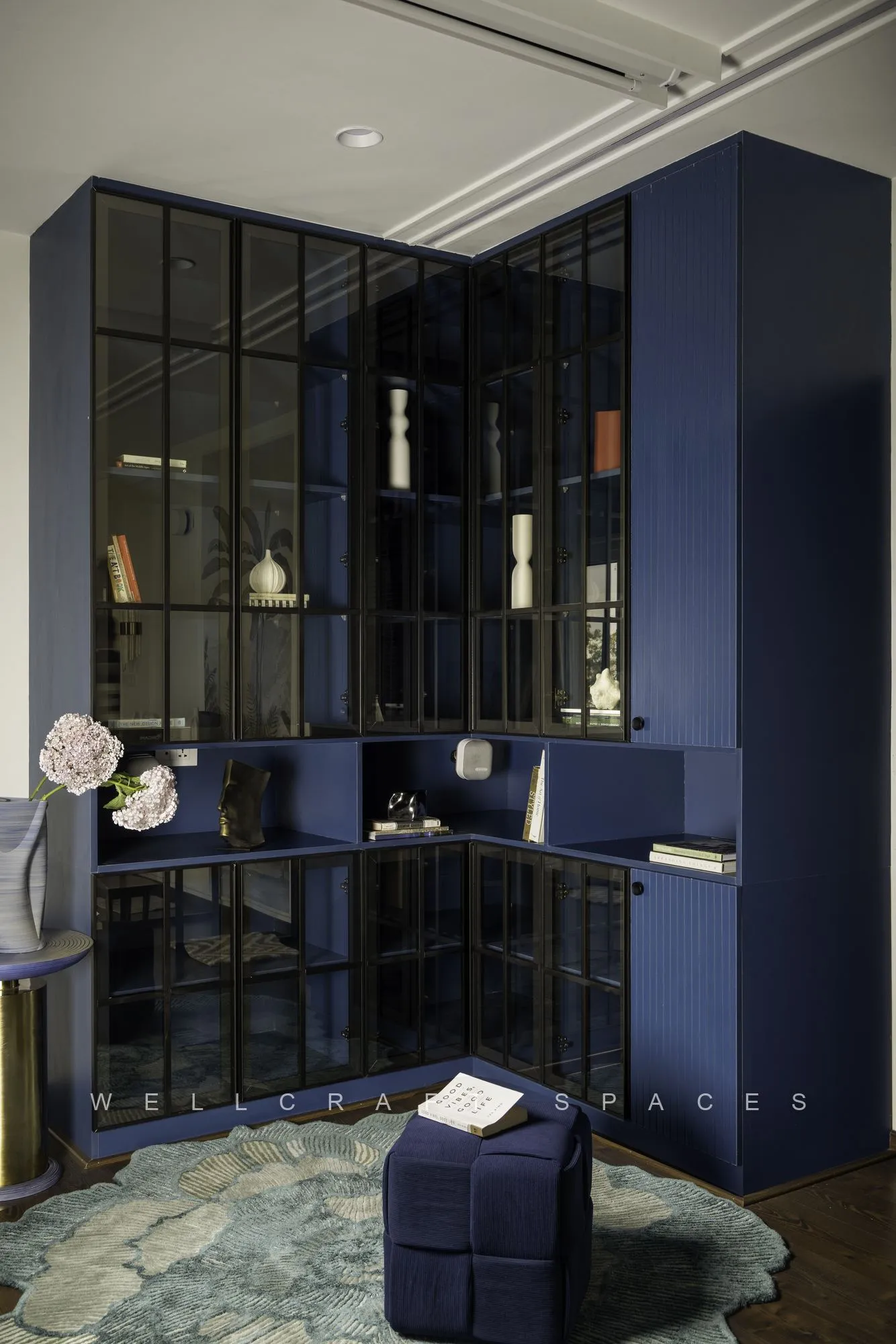 Study with a cobalt blue glass-fronted library wall, a matching blue tub chair and a blue-green patterned rug.
