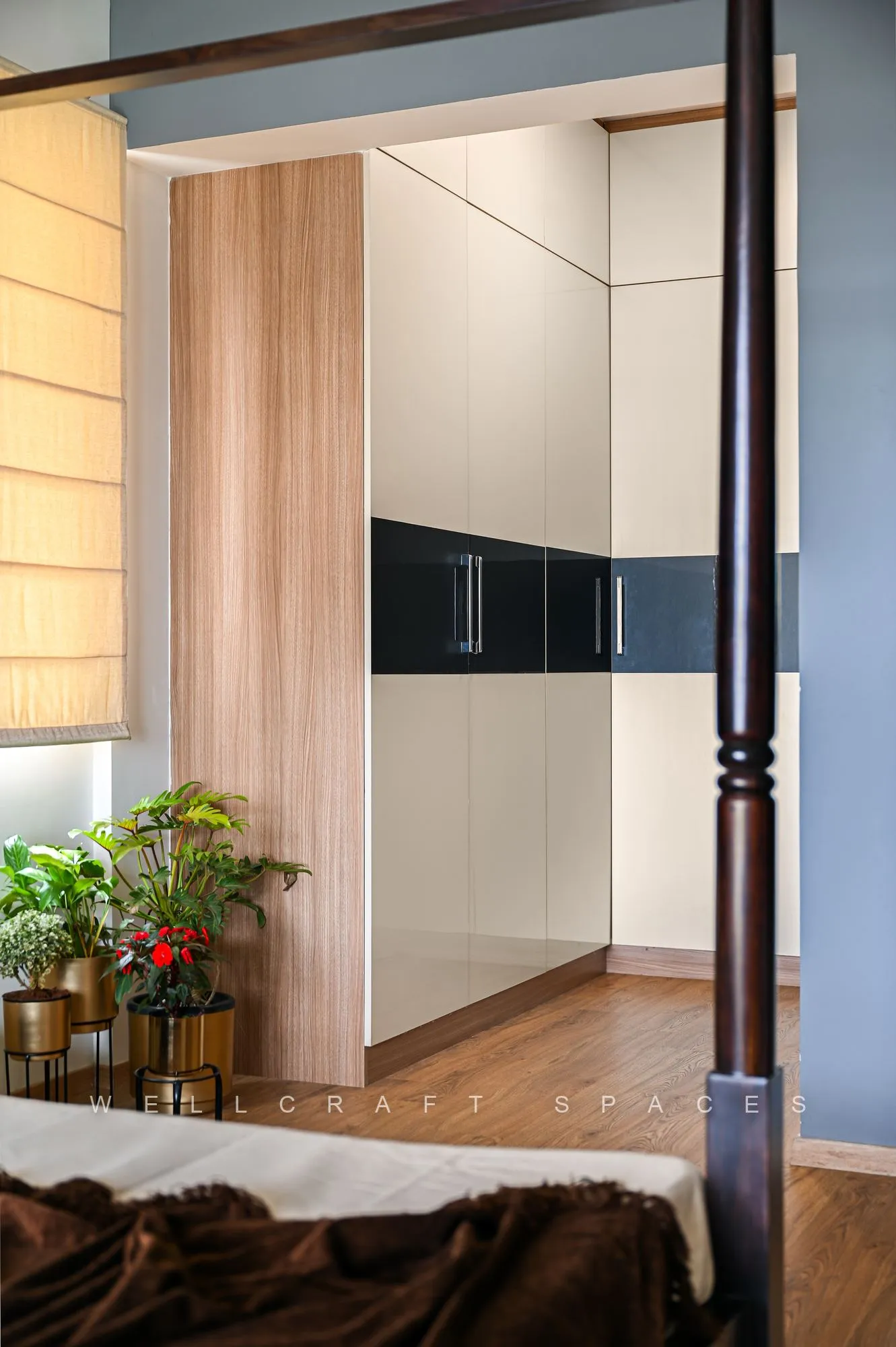 Bedroom wardrobe run in cream with a black glossy band, a wood-panelled wall alongside and brass planters by the doorway.