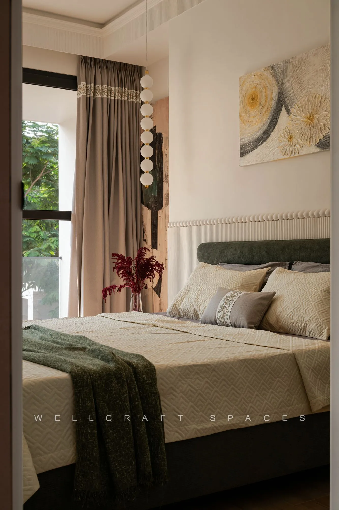 Bedroom in muted green with a studded headboard, layered throw, arched wall art and curtains drawn over a corner window.