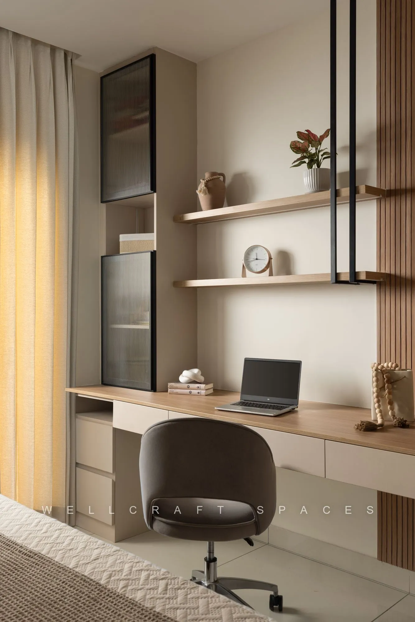 Study desk in pale oak with a black metal shelving frame, fluted wall panel and a grey upholstered swivel chair.