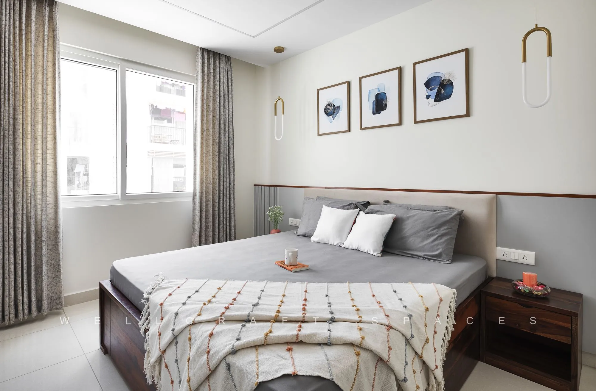 Guest bedroom with a low teak bed, a trio of framed botanical prints and a brass wall sconce beside the curtained window.