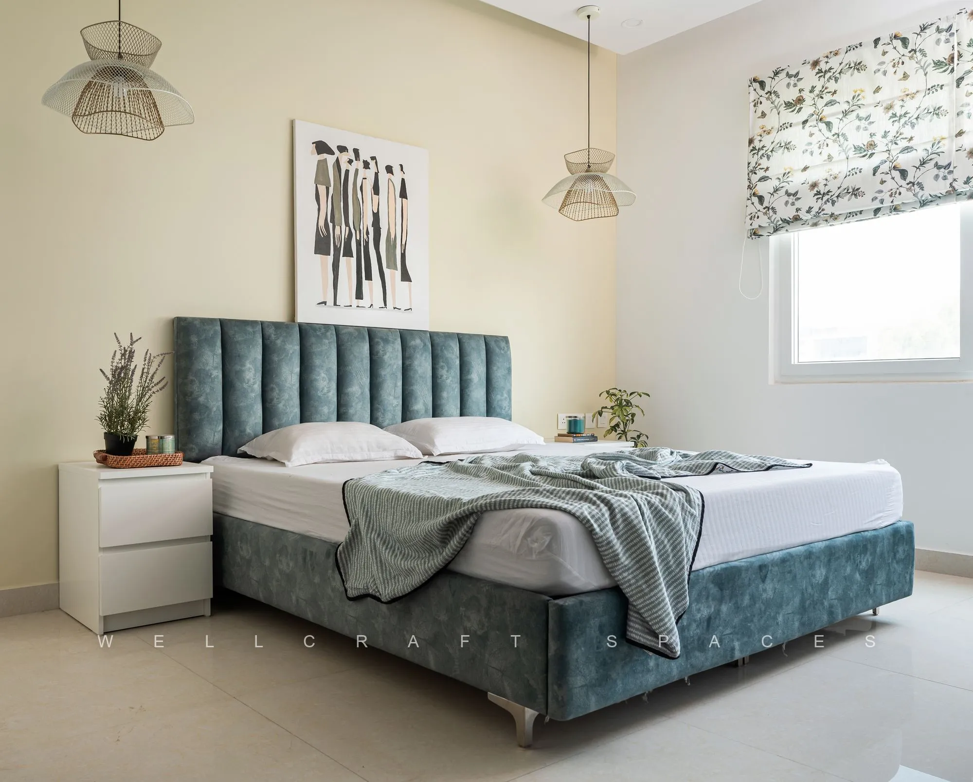 Bedroom with a teal velvet channel-tufted bed, grey throw, white bedside chests and a pair of black wire pendant lights either side.