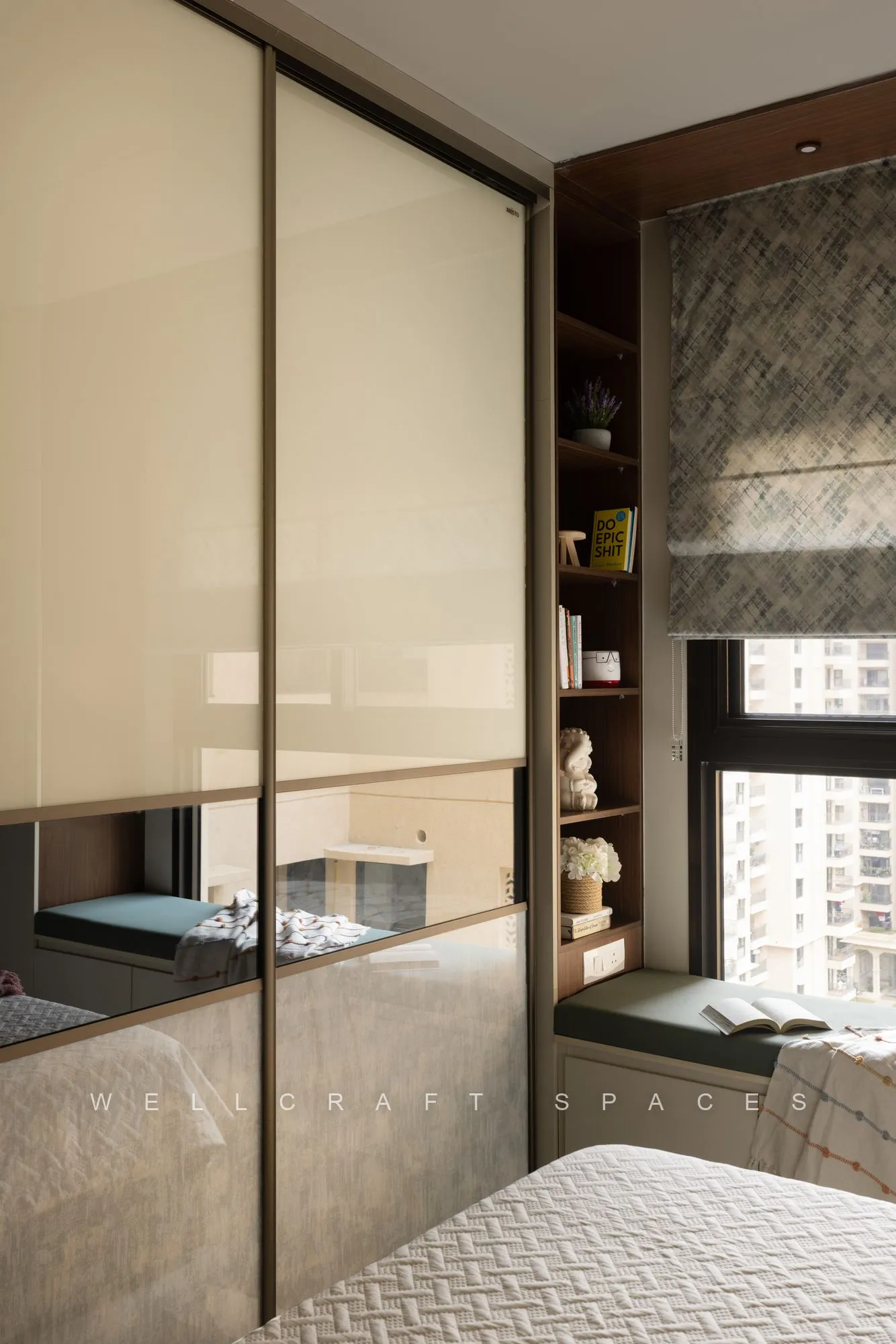 Mirrored sliding wardrobe reflecting the room, with an open teak display niche and a cushioned window seat looking outside.