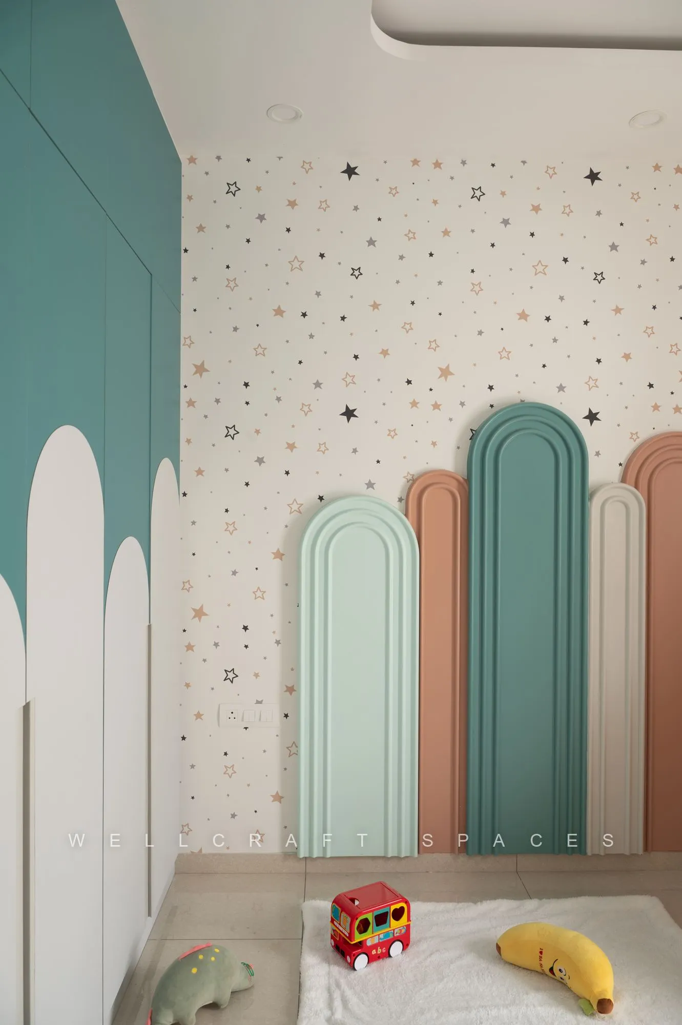 Teal tall wardrobe beside painted mint and blush arches on a star-speckled wall, with toys on a pale play mat.