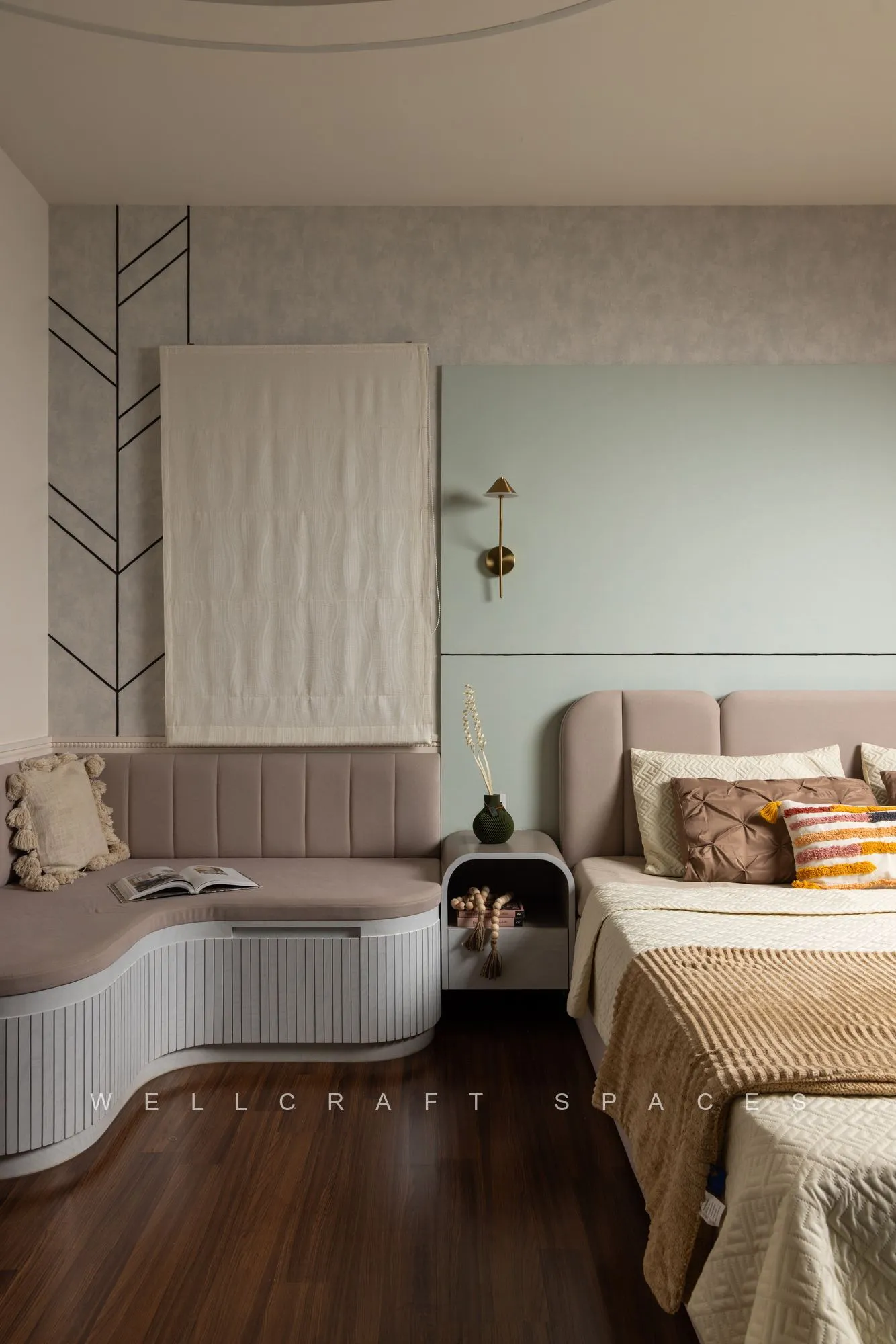 Bedroom with a blush curved headboard and rounded side table, patterned bedding and a fluted panel wall on dark timber flooring.