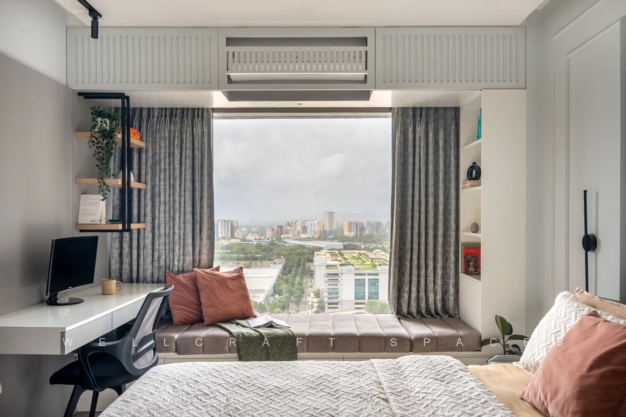 Bedroom with a built-in white study counter along the window, striped curtains and a rust-cushioned bed, looking out over the skyline.