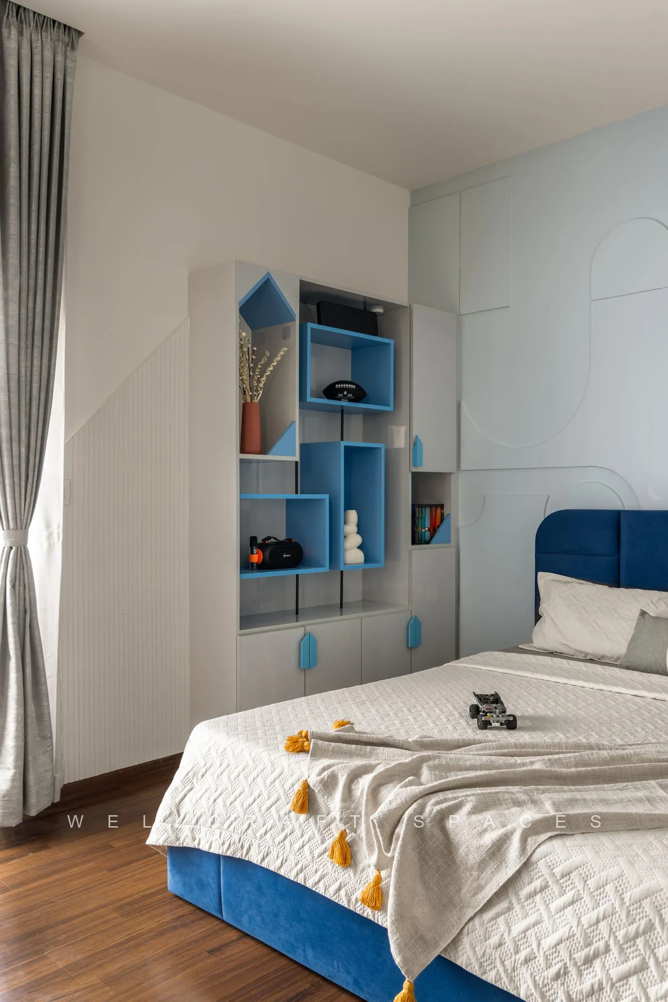 Kids bedroom with a royal blue upholstered bed, geometric blue open shelving and a white panelled wall with toys on display.
