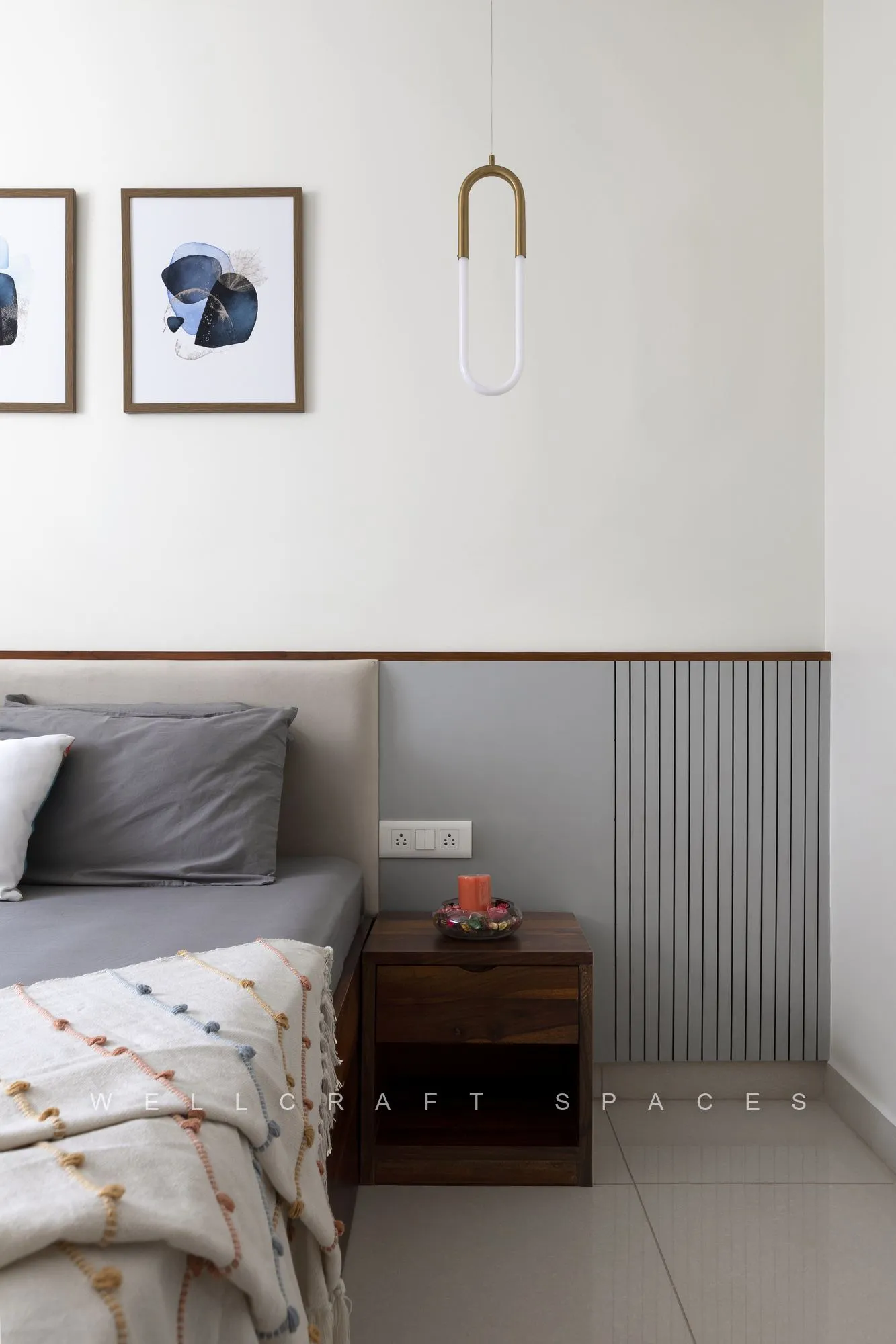 Bed set against grey fluted wainscoting with a teak ledge, framed indigo artwork and a capsule-shaped wall light.