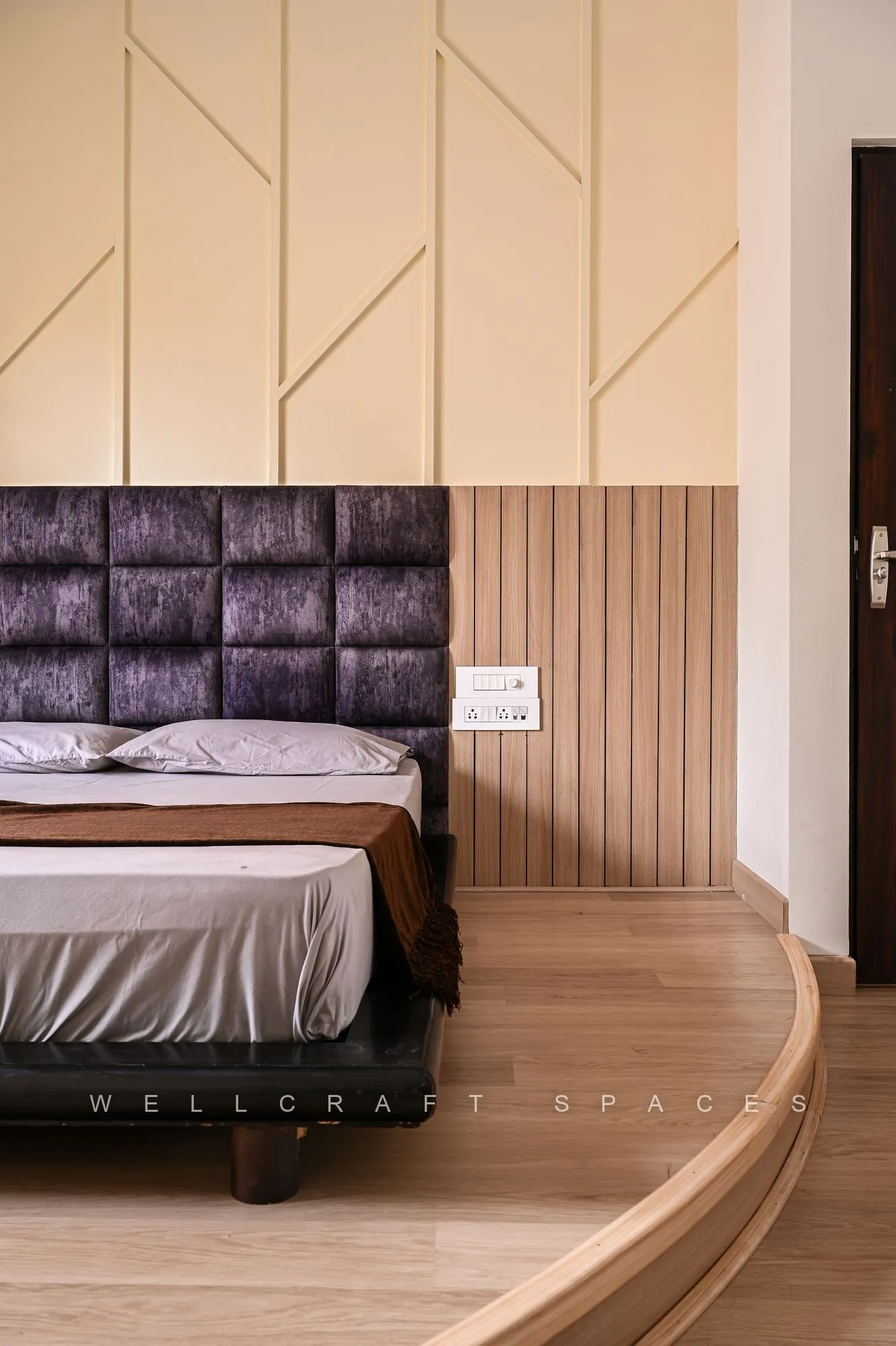 Bedroom with a buttoned dark leather headboard set into ribbed oak panelling, cream linen bedding and a geometric inlay wall behind.