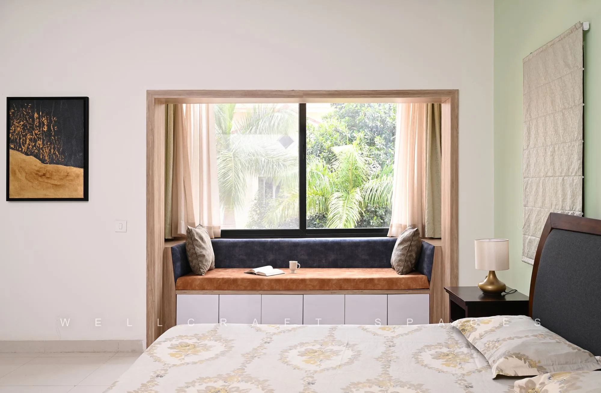 Guest bedroom with a cushioned window seat overlooking greenery, an ivory patterned bedspread and soft sage walls.